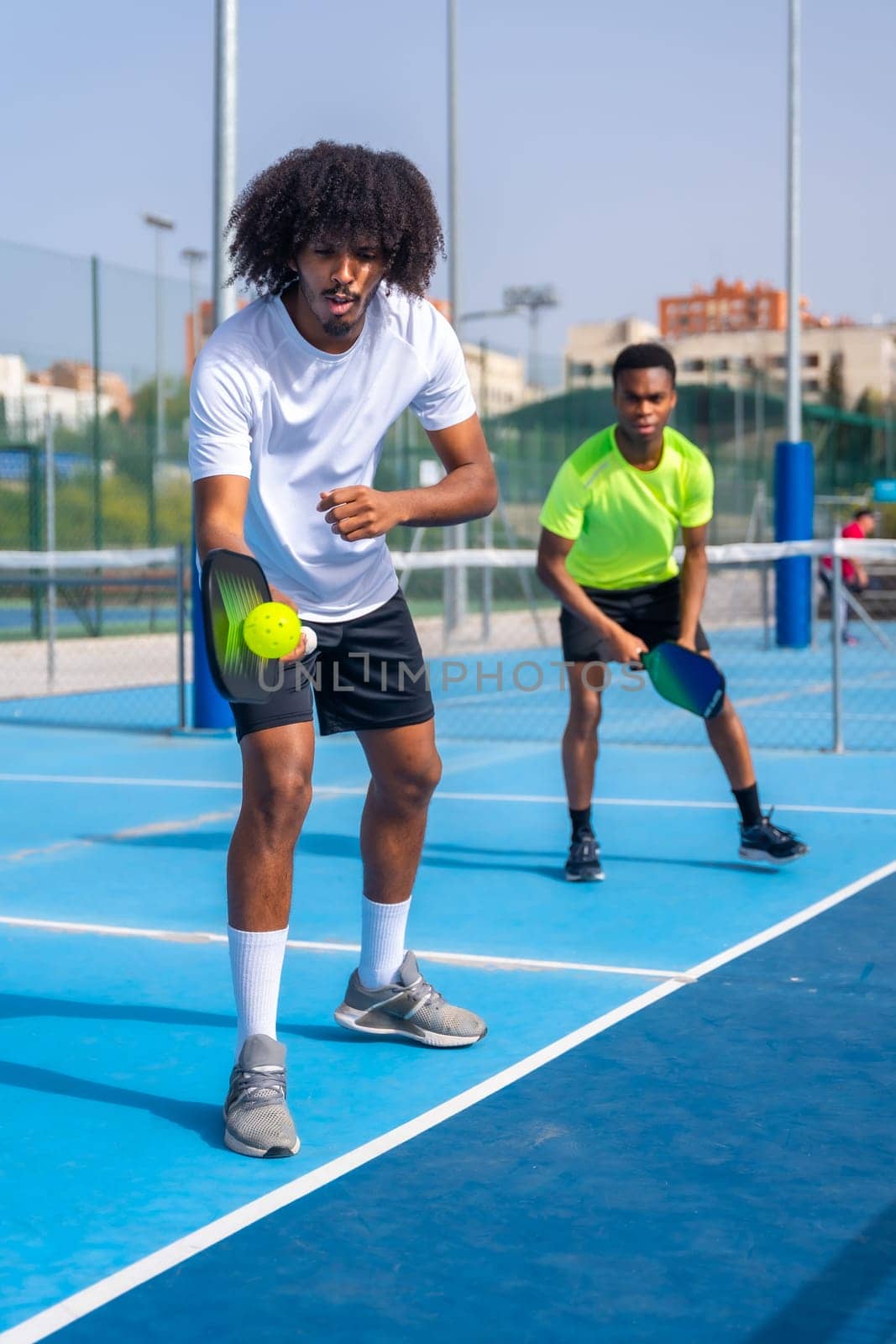 Vertical full length photo of an african sportive man serving ball during pickleball match outdoors