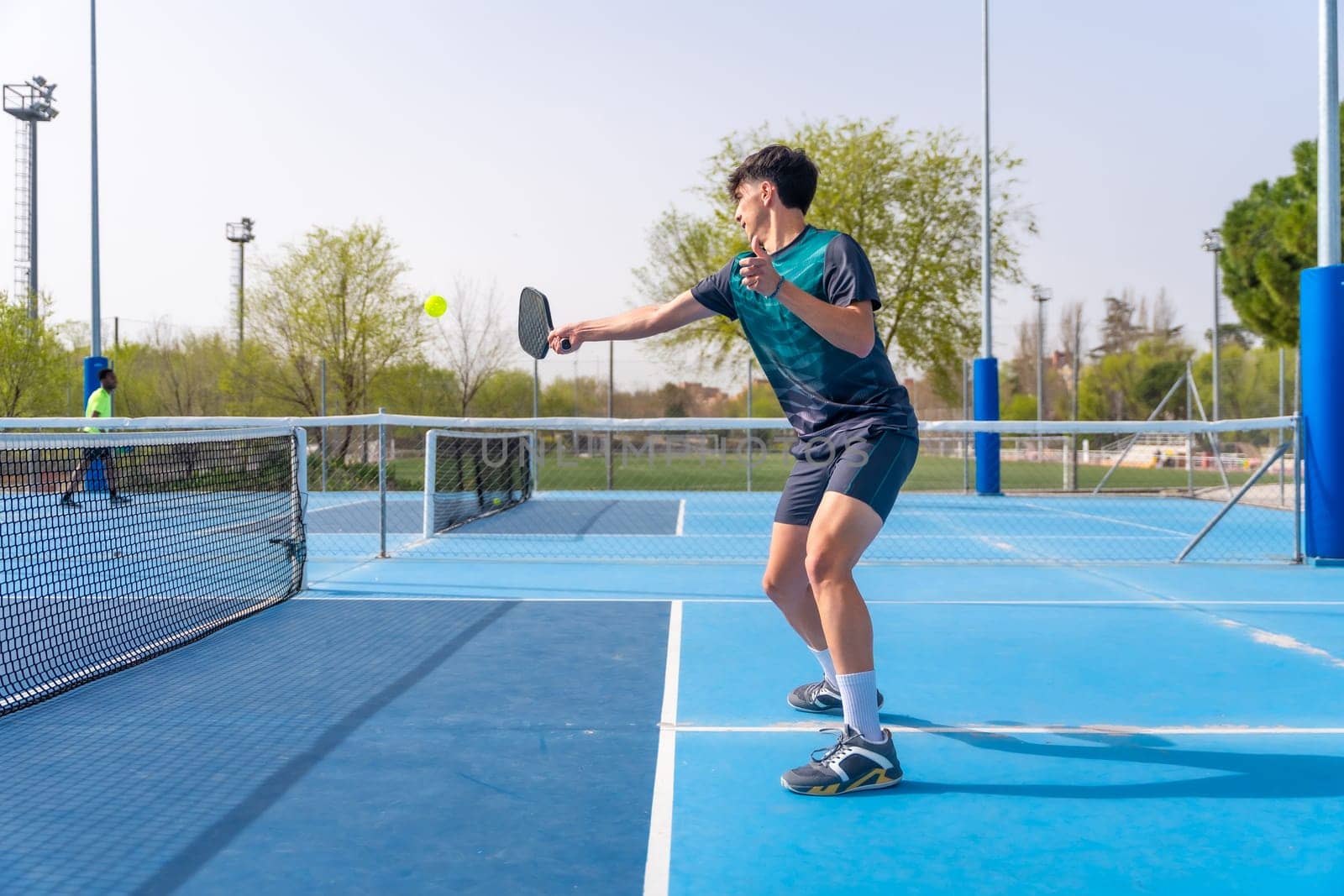Young fit man playing pickleball in an outdoor court by Huizi