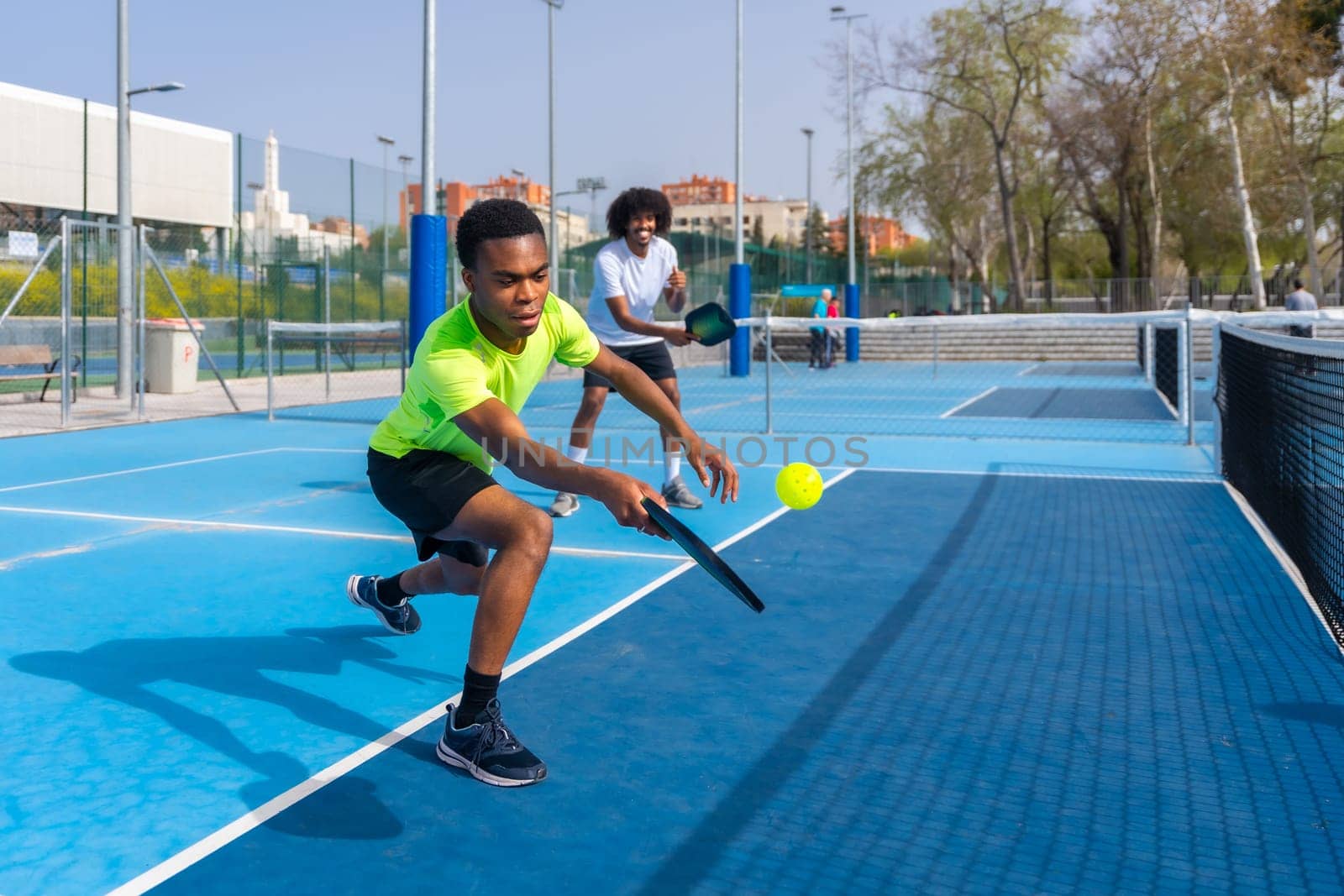 Man running to reach a ball playing pickleball with friend by Huizi