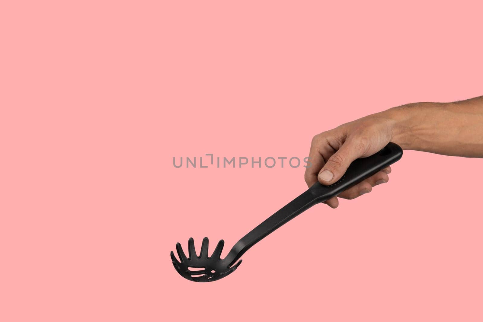 Black male hand holding plastic kitchen skimmer on pink background. High quality photo