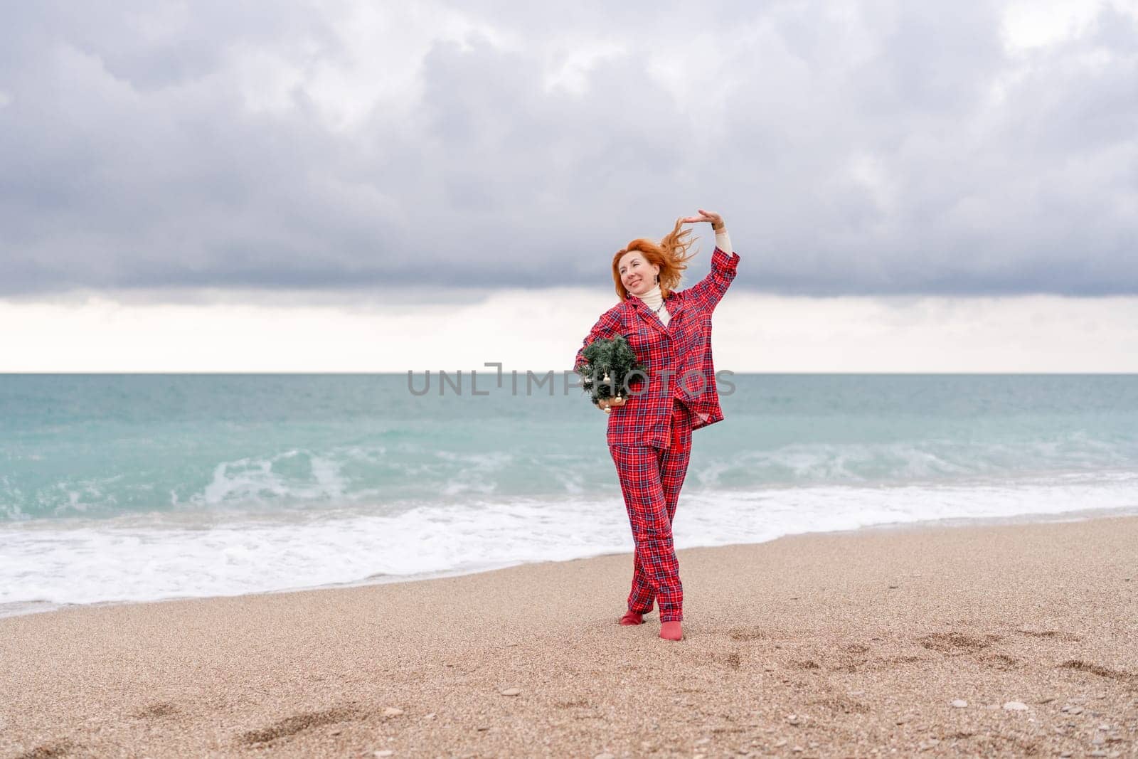 Sea Lady in plaid shirt with a christmas tree in her hands enjoys beach. Coastal area. Christmas, New Year holidays concep.