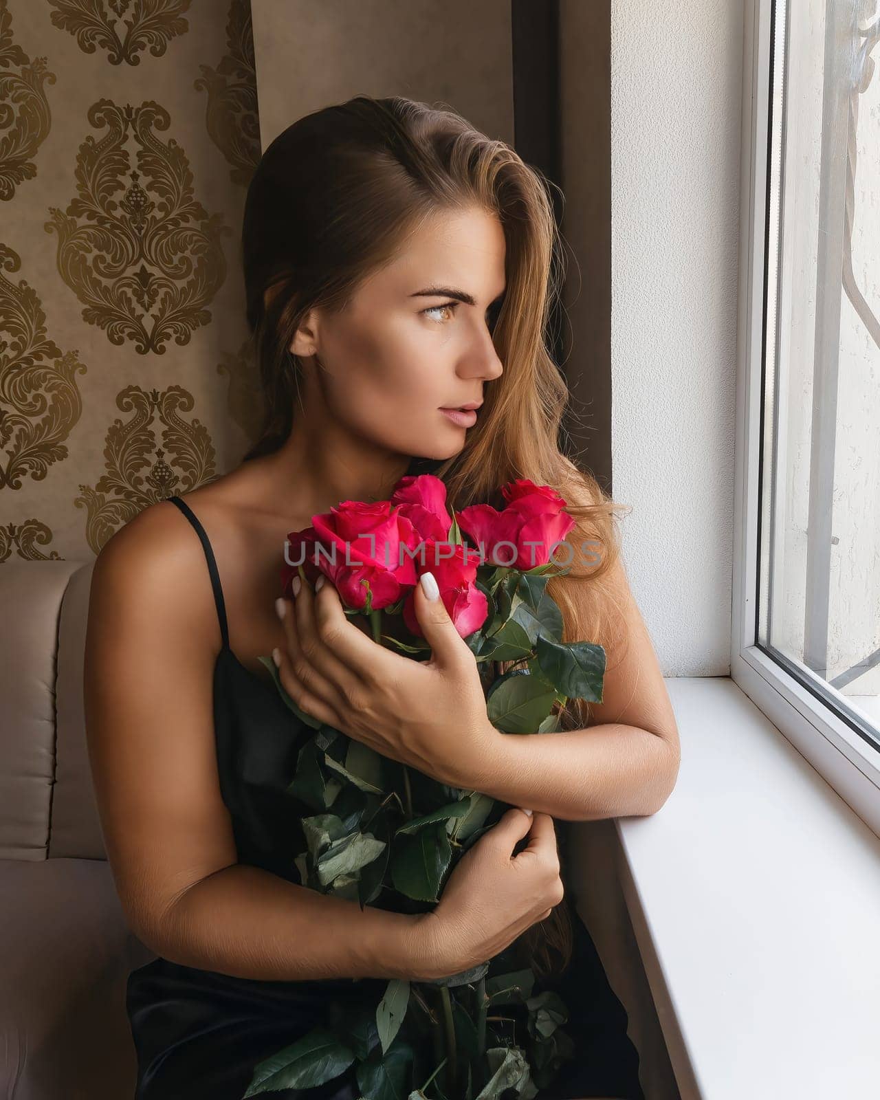 A woman in a black dress is sitting in front of a window with a bouquet of red roses. by Matiunina