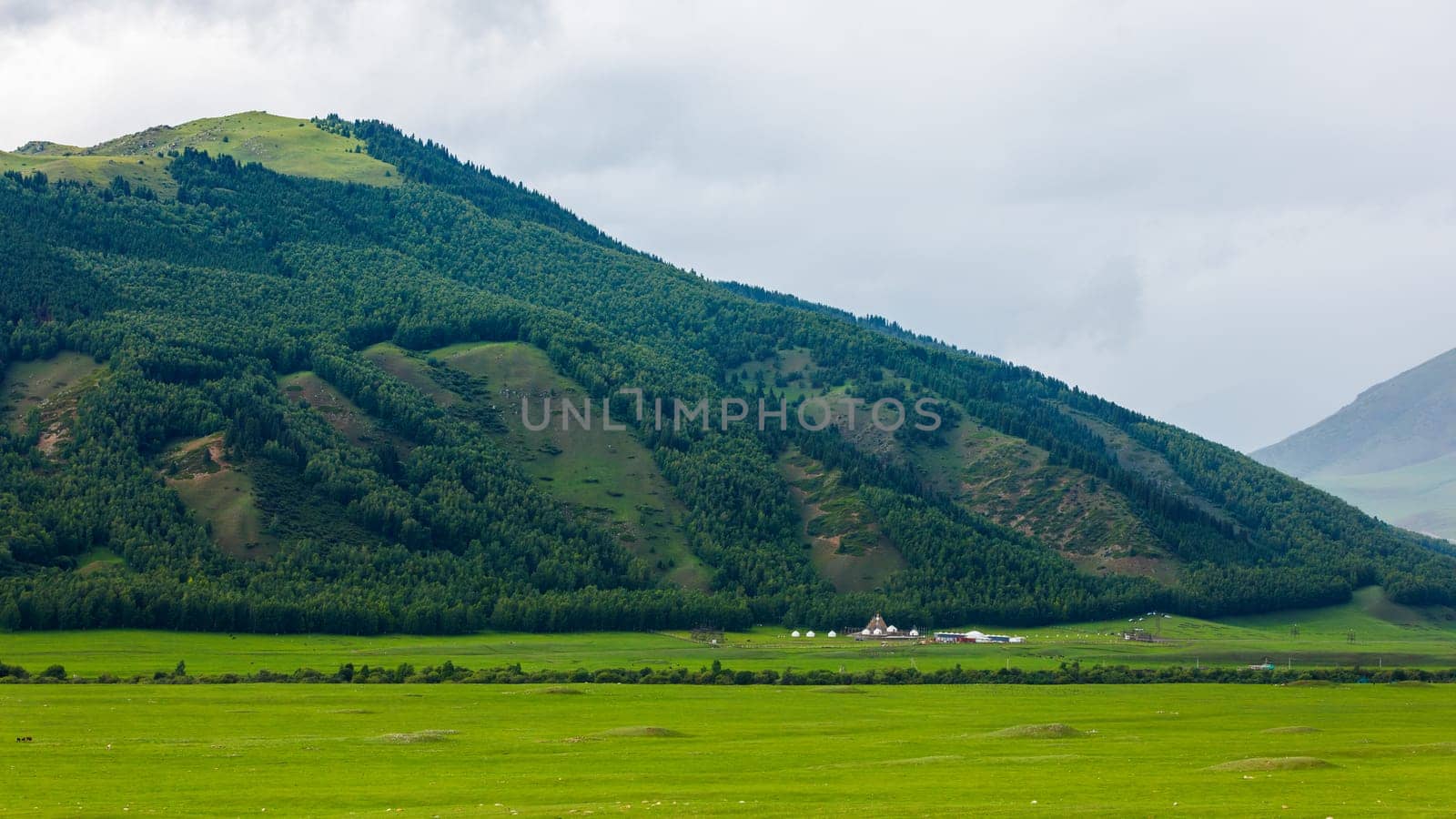 Grassy field in foreground with a majestic mountain backdrop around Kochmon Ordo Ethno Complex Yurt Camp by z1b