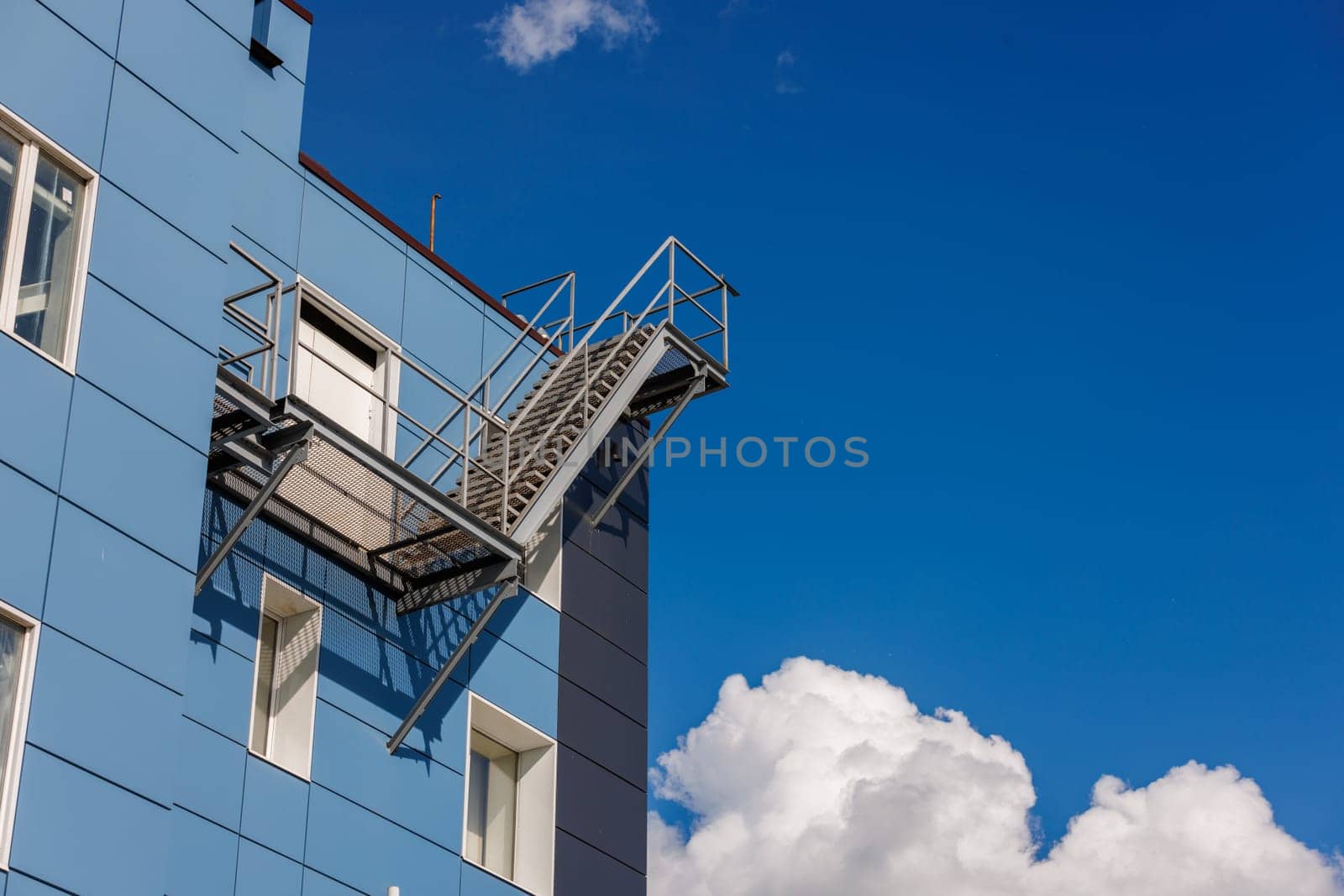 A blue office building wall with composite aluminum panels and a fire escape on the side.