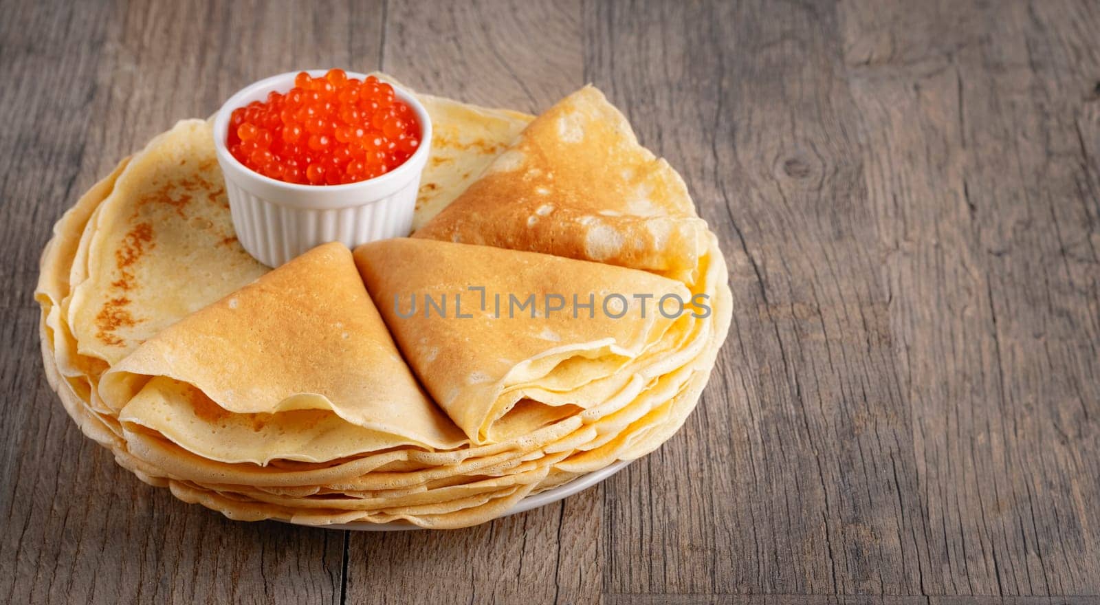 Pancakes with red caviar on a wooden table, with copy space for text.