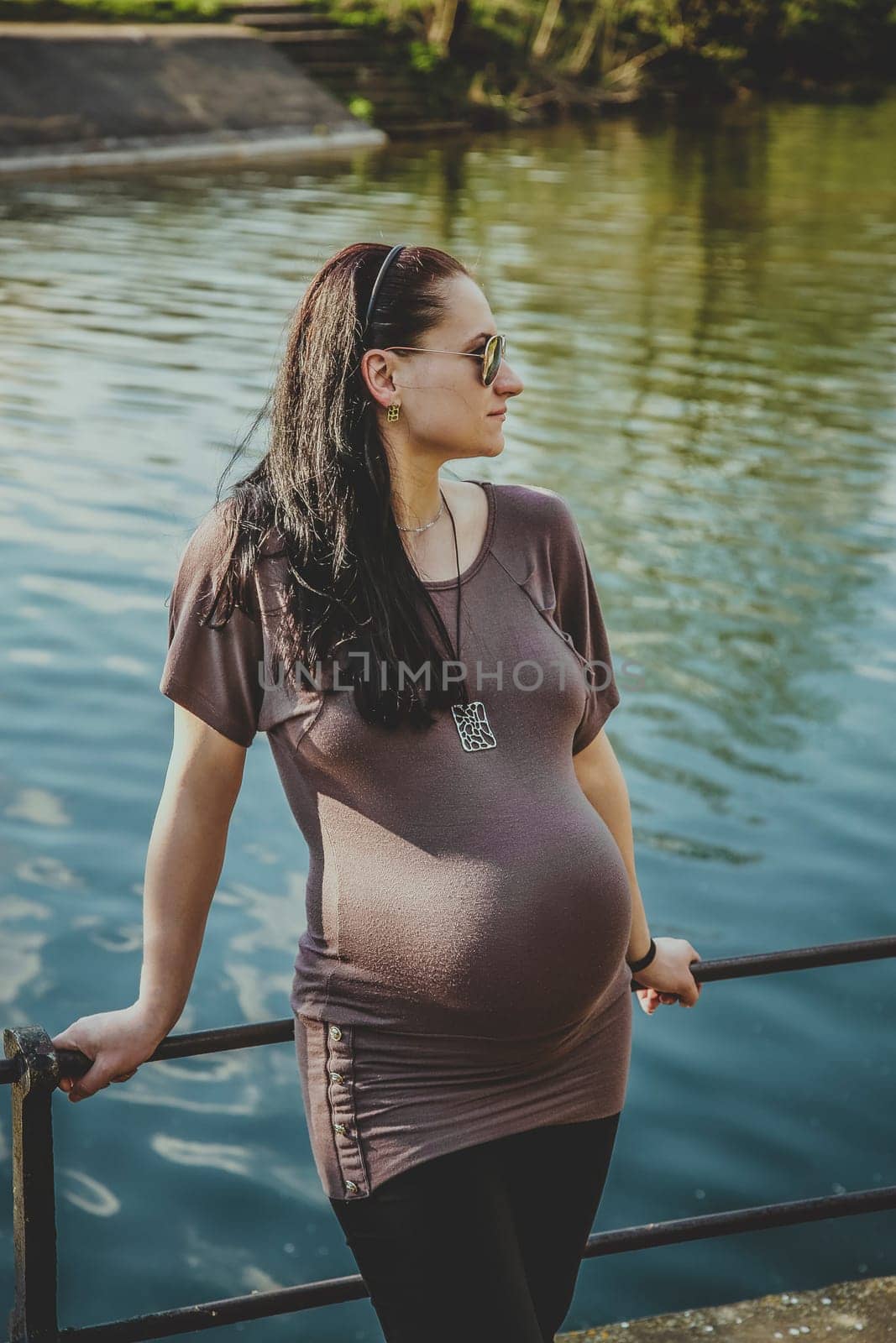 A pregnant girl on the bridge is resting on a summer day near a pond