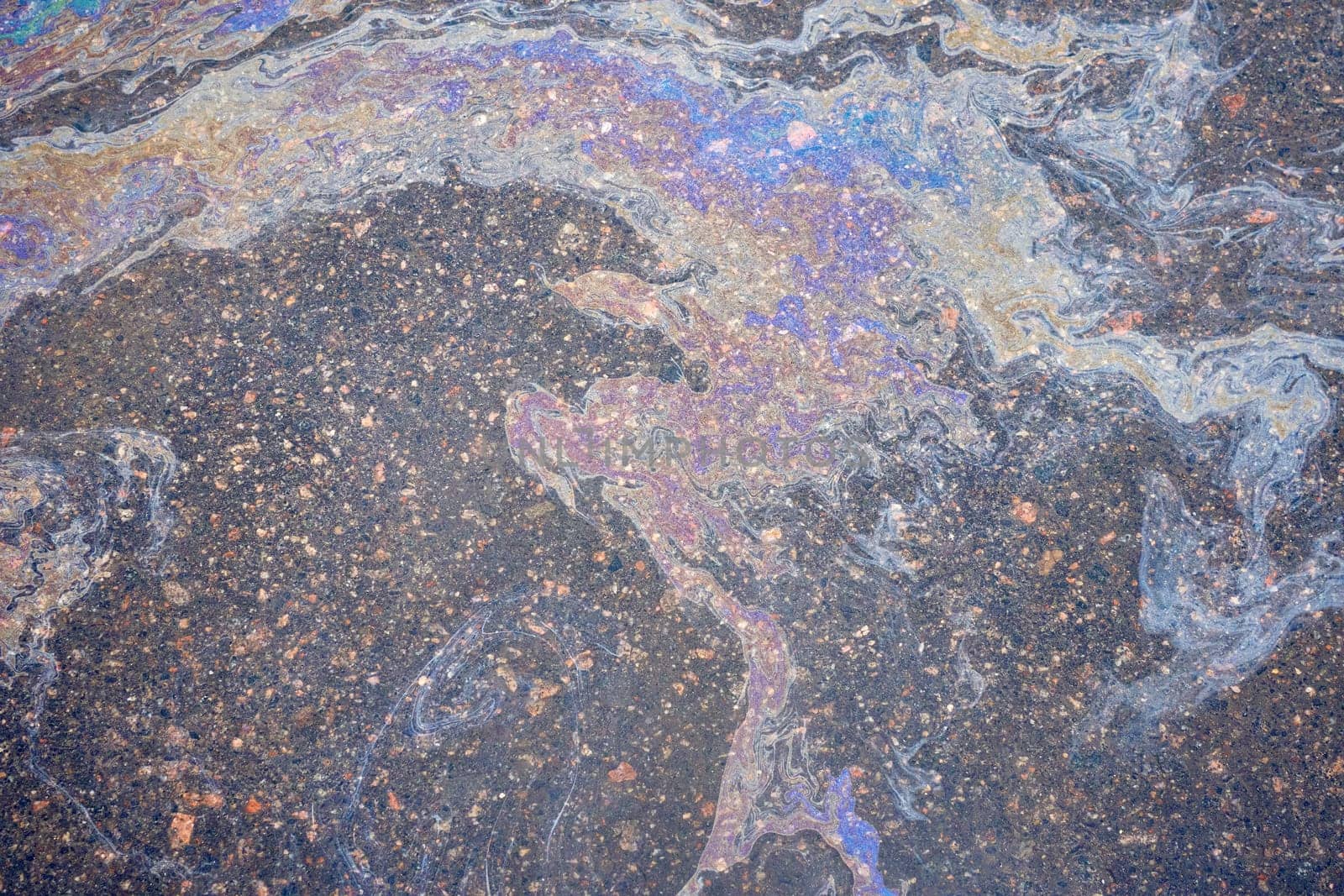 Oil residues on wet asphalt interact with sunlight, displaying a rainbow-like spectrum of colors. by AliaksandrFilimonau