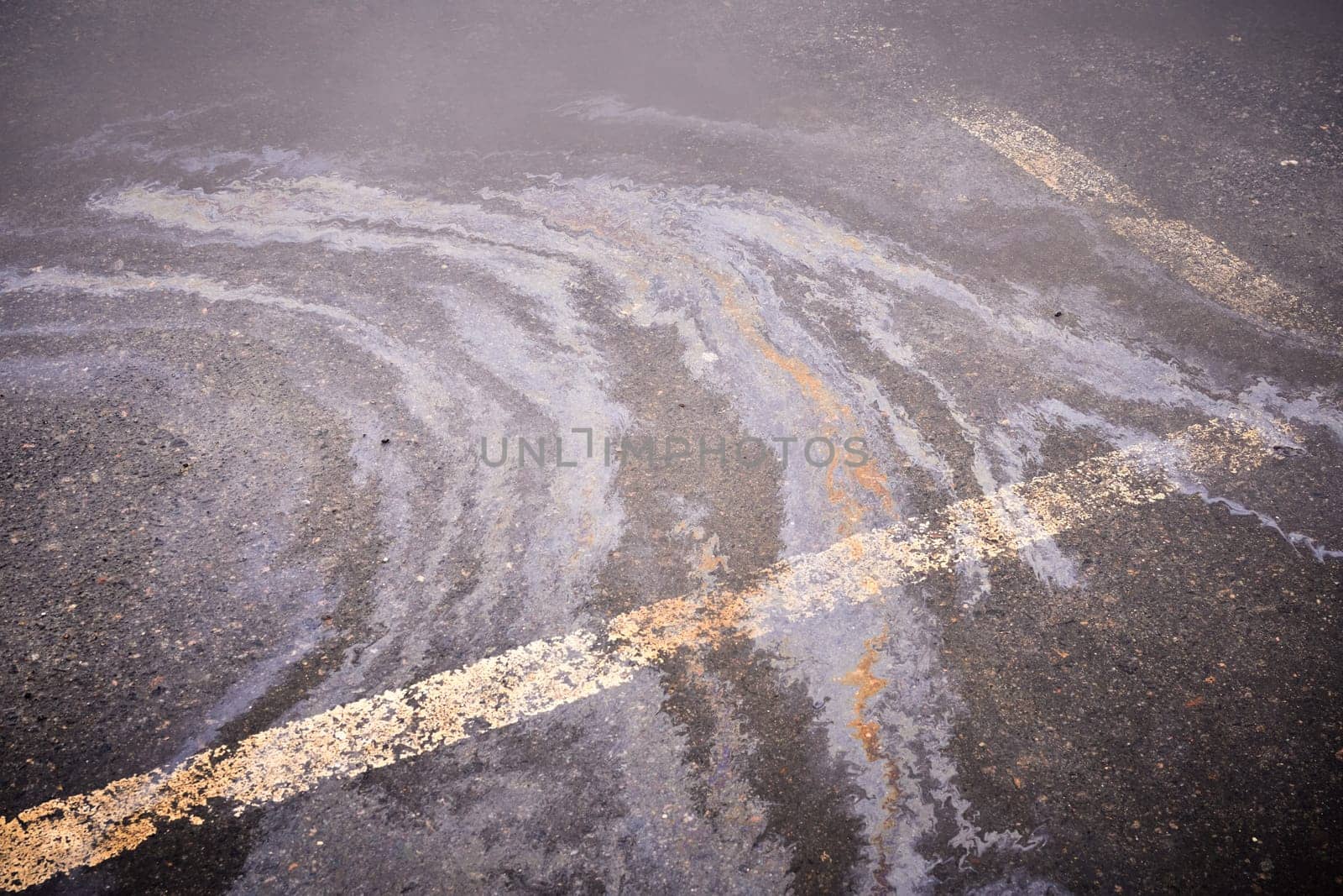 Oil spill on wet asphalt, parking lot with dividing line. Environmental problems of water pollution