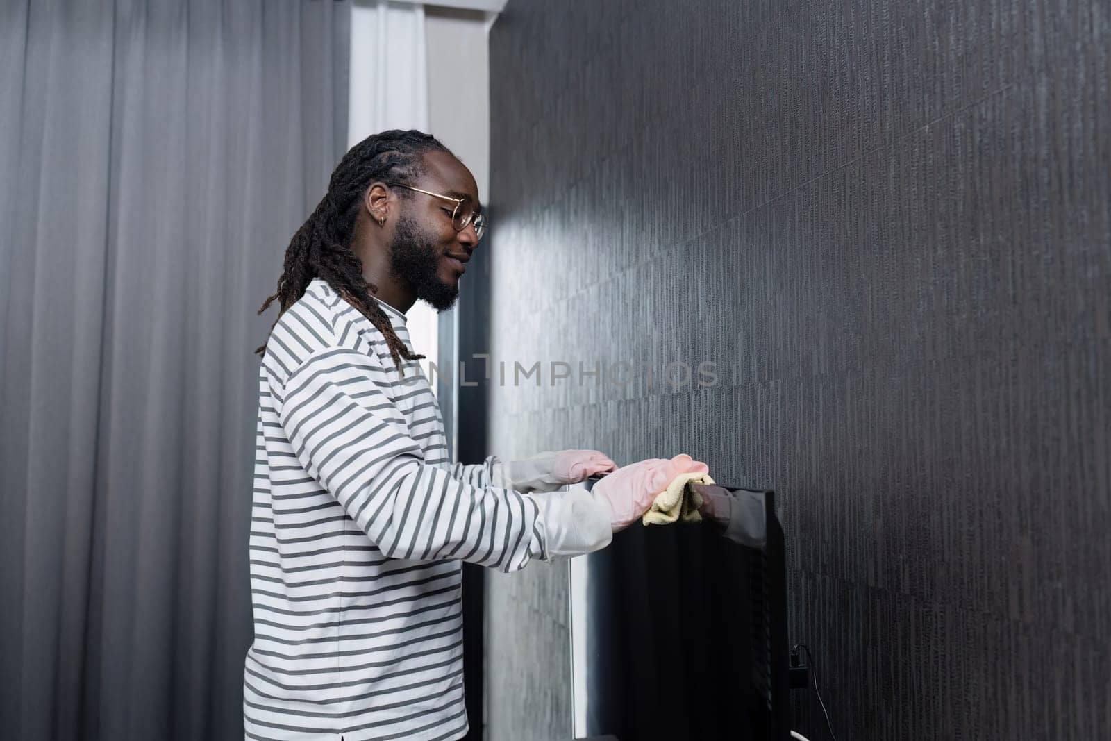 African American man doing housework at home on weekend, cleaning the living room, butler wiping the TV with a microfiber cloth.