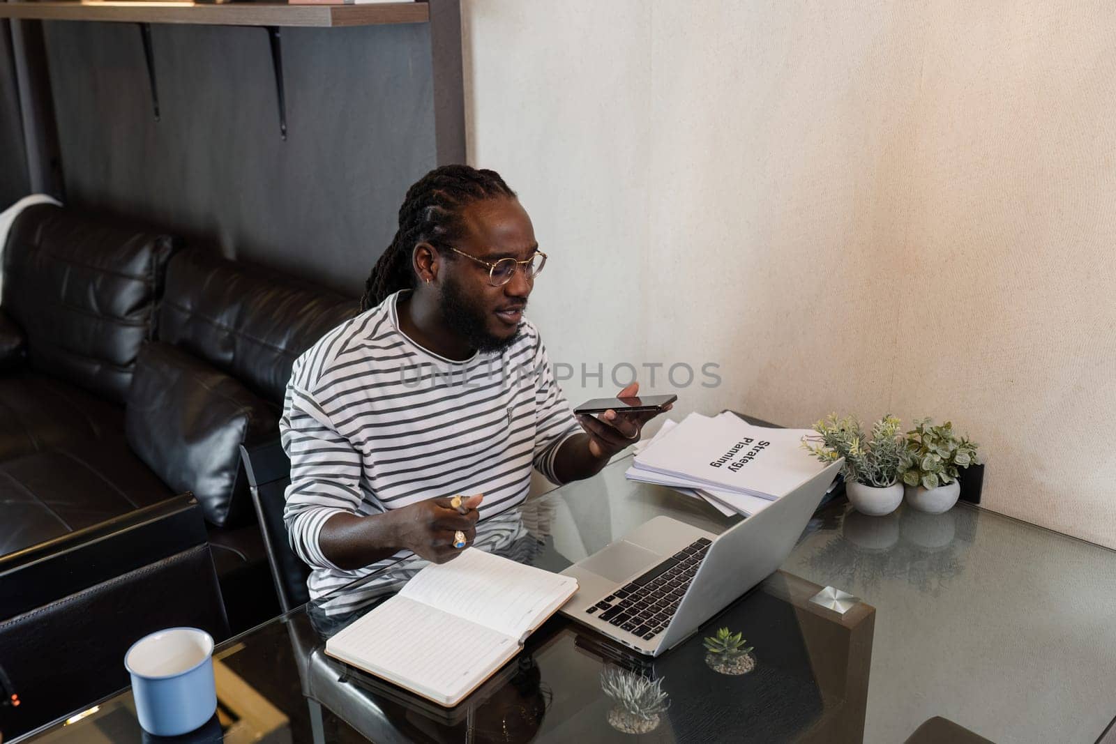 Young African American business man working with laptop and document on desk and talking on mobile at home.