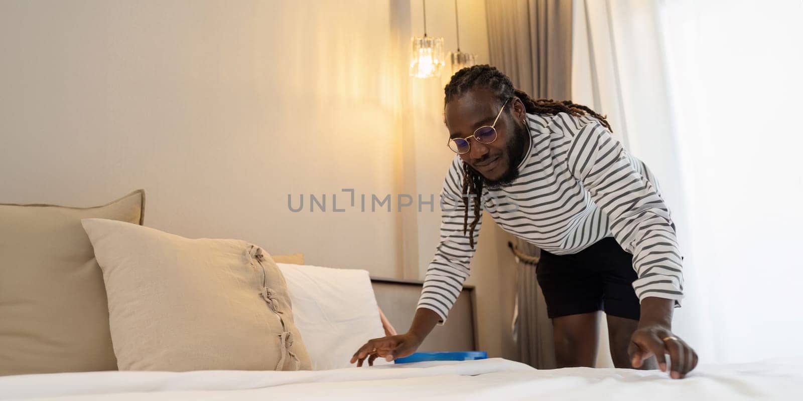 African American man doing housework at home on weekend, cleaning bed and cleaning bedroom.