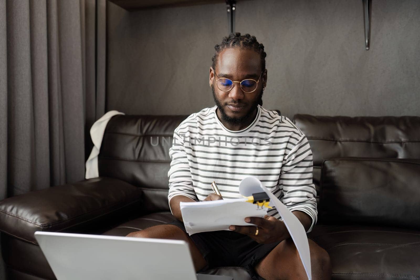 African American man working with document and laptop at home on couch. work from home concept.