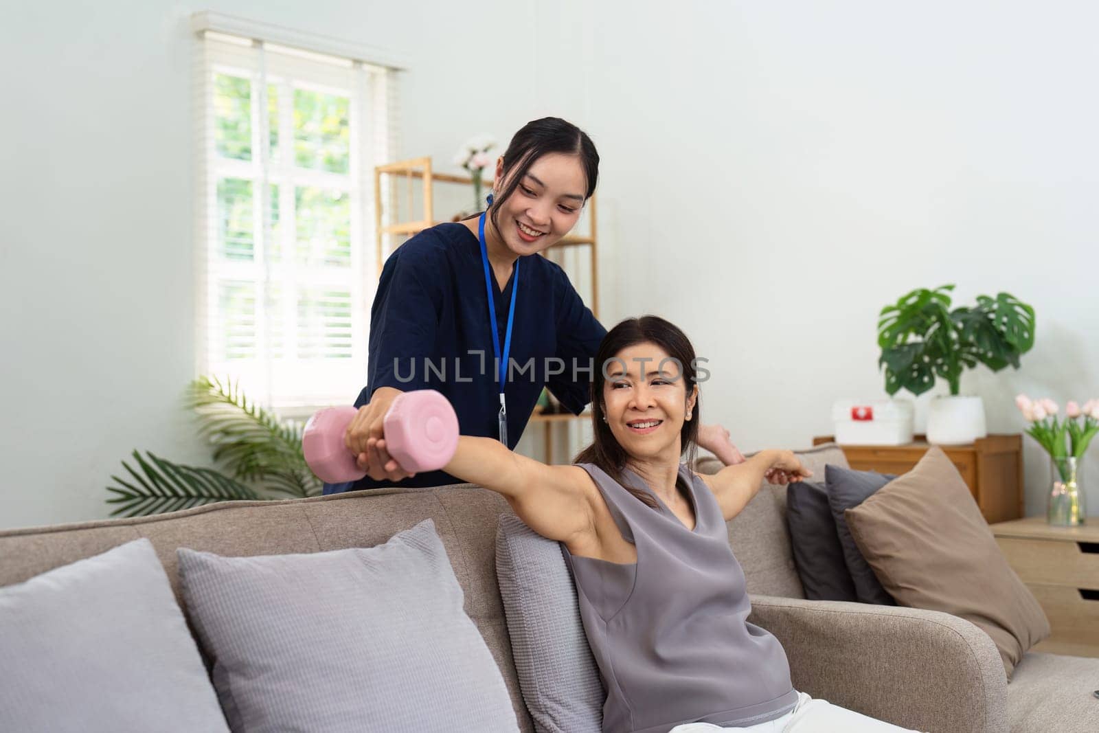 Asian older aged woman doing physiotherapist with support from nurse. Therapist assisting senior woman with exercises in nursing home.