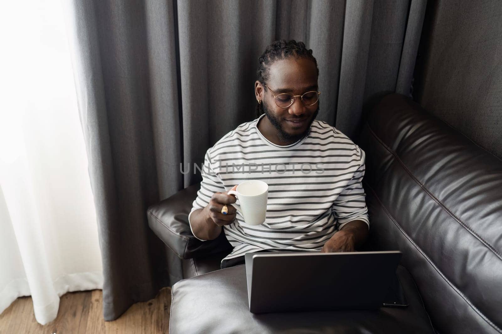 African American businessman working from home, working on laptop and drinking coffee and relax while working from home.