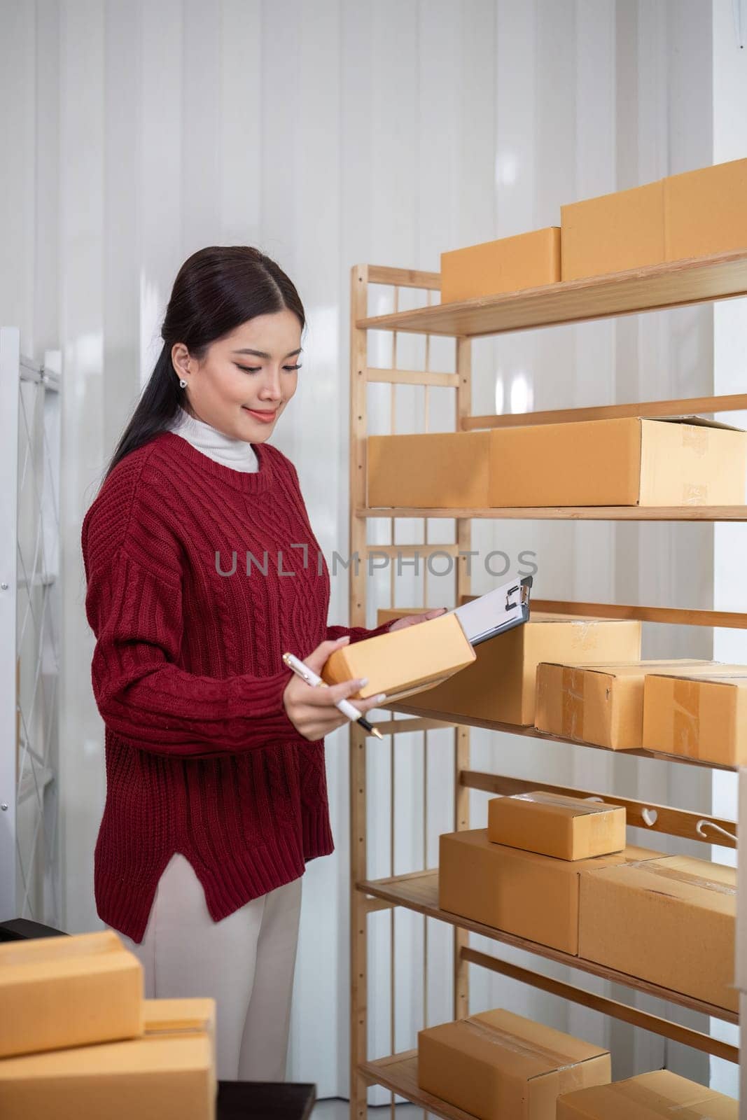 A female Asian online business entrepreneur prepares and packs merchandise into parcel boxes on a table to deliver to customers..