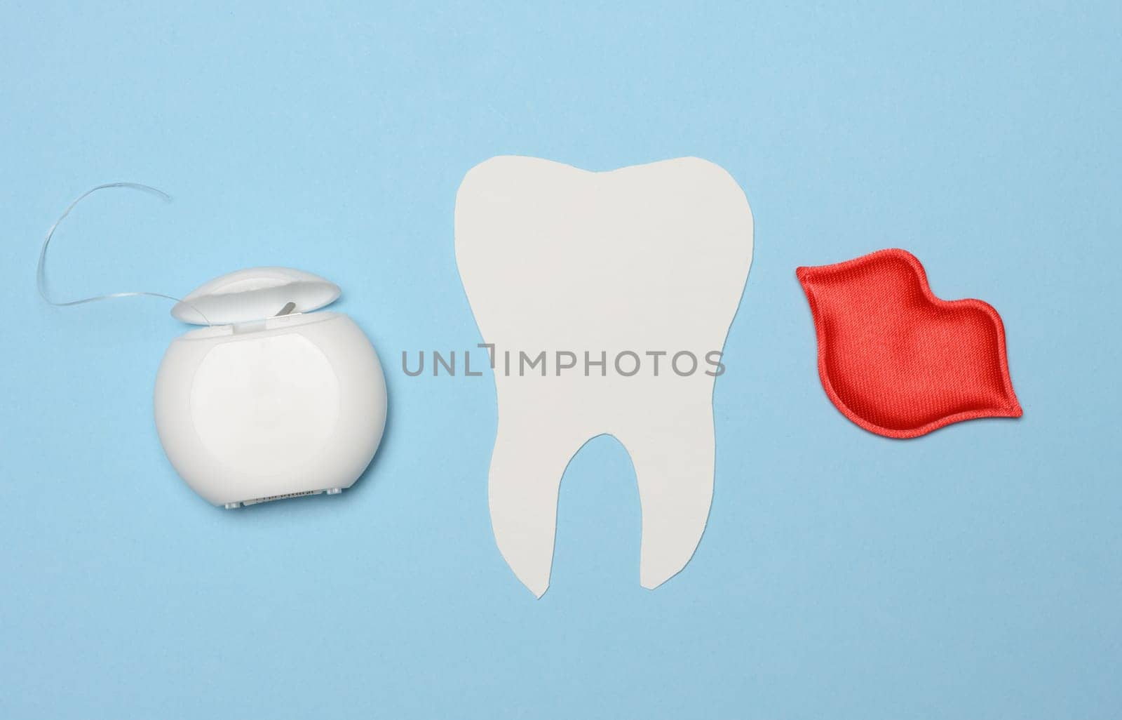 Dental floss and paper tooth on blue background, oral hygiene