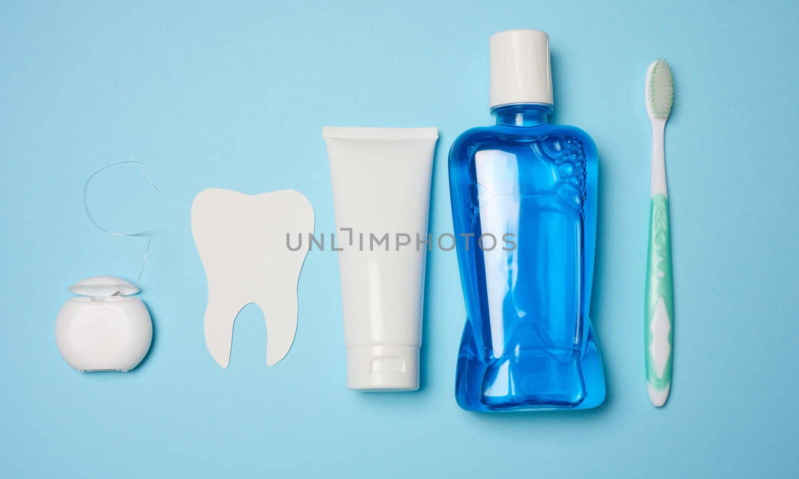 Mouthwash, toothpaste tube, dental floss on a blue background, oral hygiene, flat lay