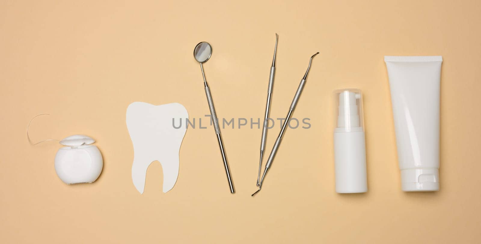 Dental mirror, tube of toothpaste and dental floss on a brown background, top view