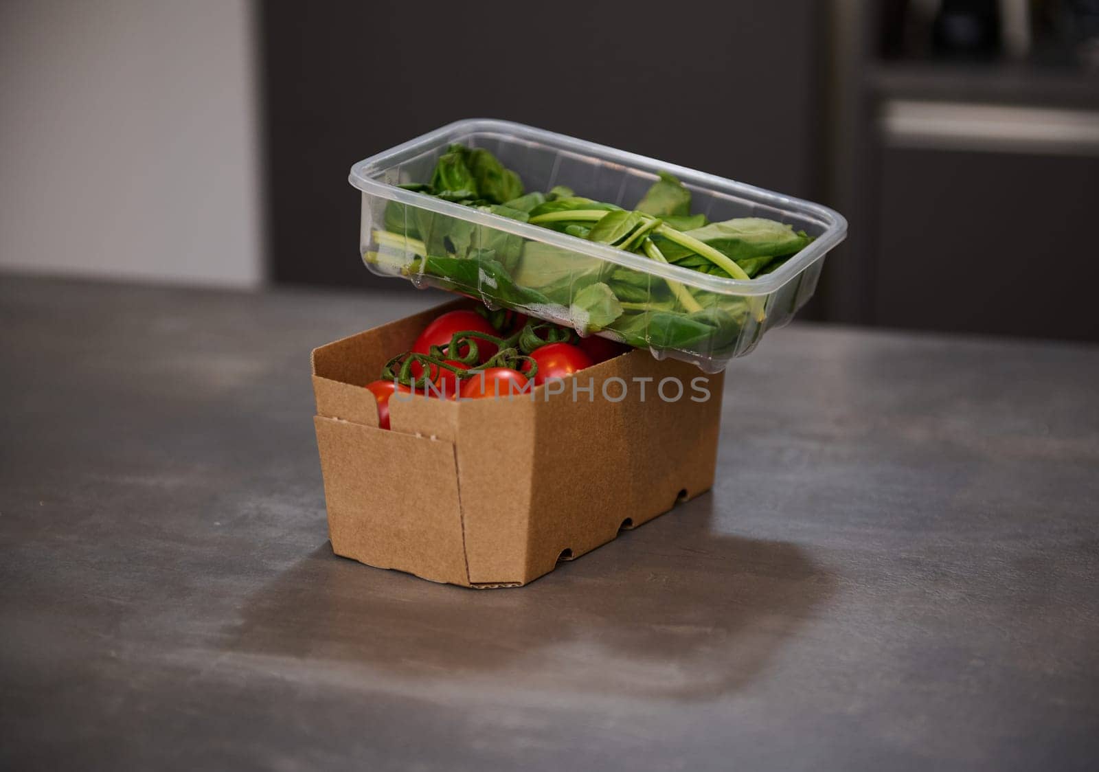 Fresh organic tomatoes cherry and arugula green leaves in recyclable paper box on a gray surface of kitchen table. Healthy eating. Vegetarian food. Fresh ingredients for wholesome salad