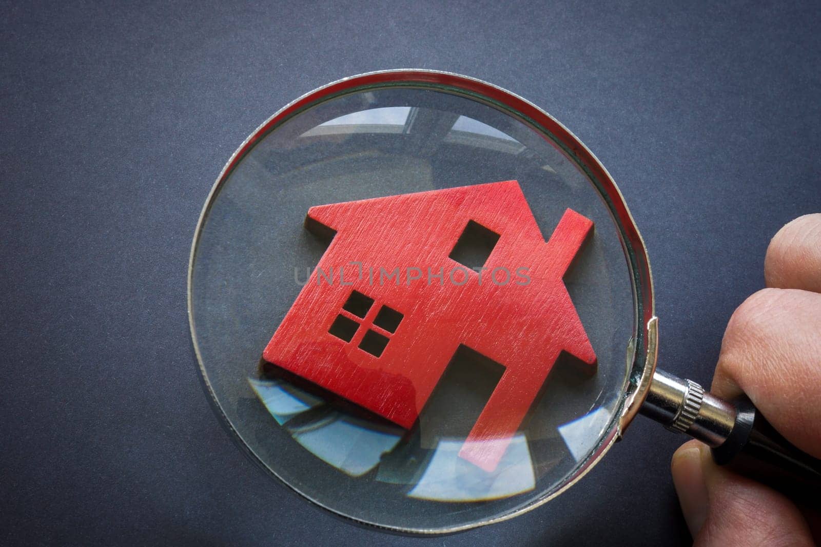 Property valuation. A figurine of a house and a hand with a magnifying glass. by designer491