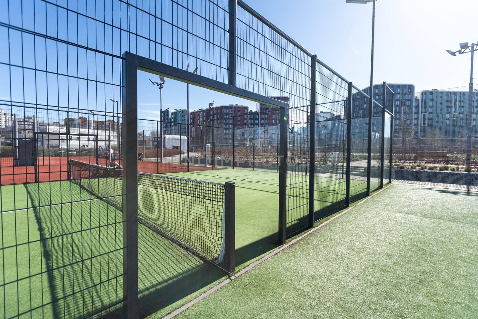 Landscaped areas of a residential development with a tennis court with high Plexiglas and metal fences. High quality photo