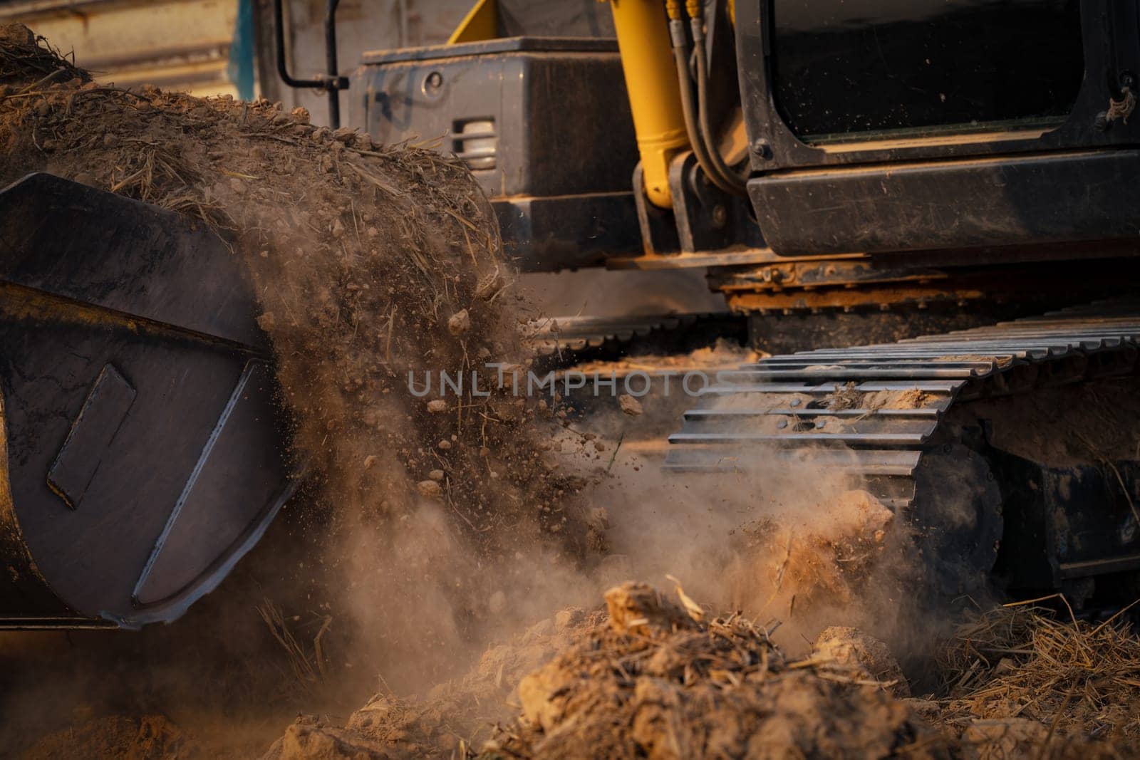Selective focus on metal bucket teeth of backhoe digging soil. Backhoe working by digging soil at construction site. Crawler excavator digging on soil. Earth moving machine. Excavation vehicle. by Fahroni