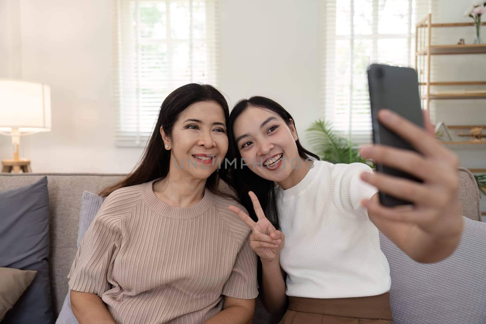 Daughter adult taking selfie using mobile phone with senior mother at home.