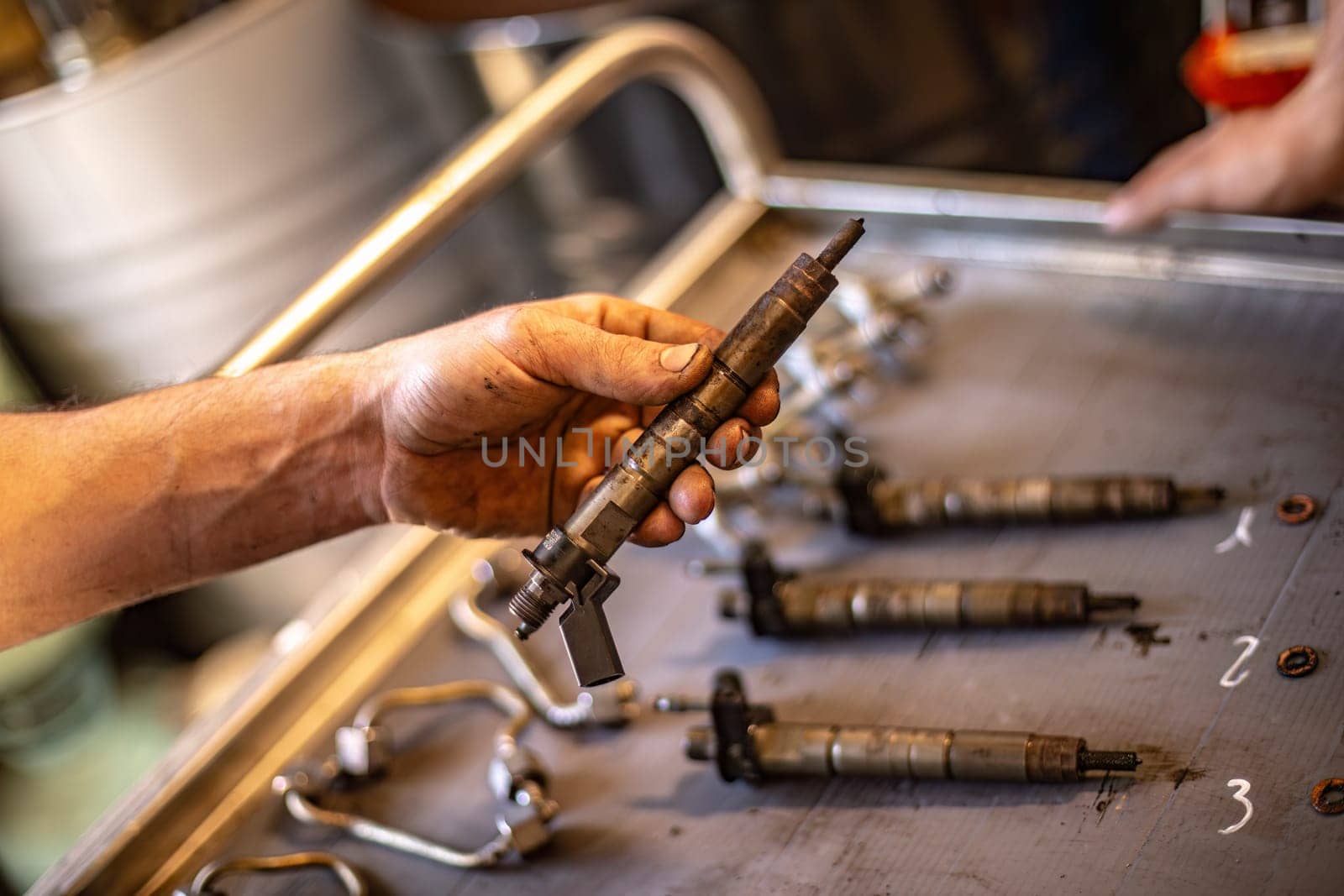 Close-up of a mechanic’s dirty hands holding a diesel engine injector, focus on repair work.