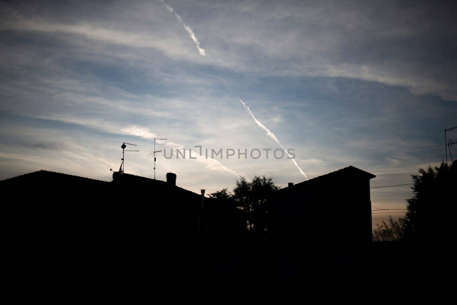 Silhouette of an urban skyline under a clear blue sky with visible contrails, merging nature and city.