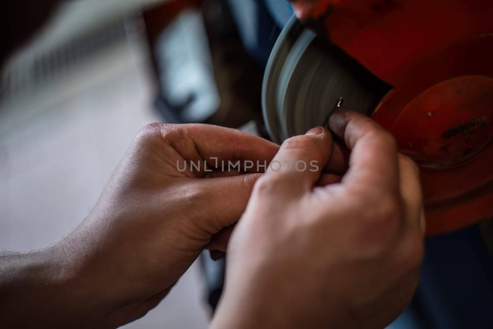 Mechanic's hands expertly sharpening a drill bit on a grinding wheel in a workshop.