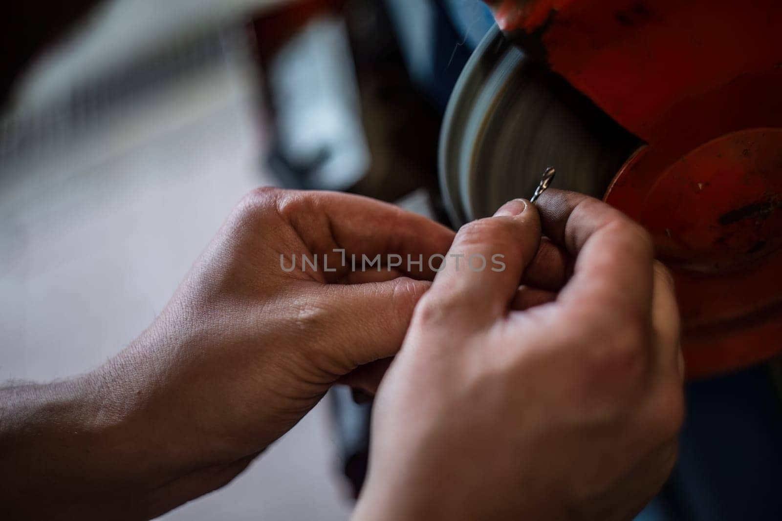 Mechanic's hands expertly sharpening a drill bit on a grinding wheel in a workshop.