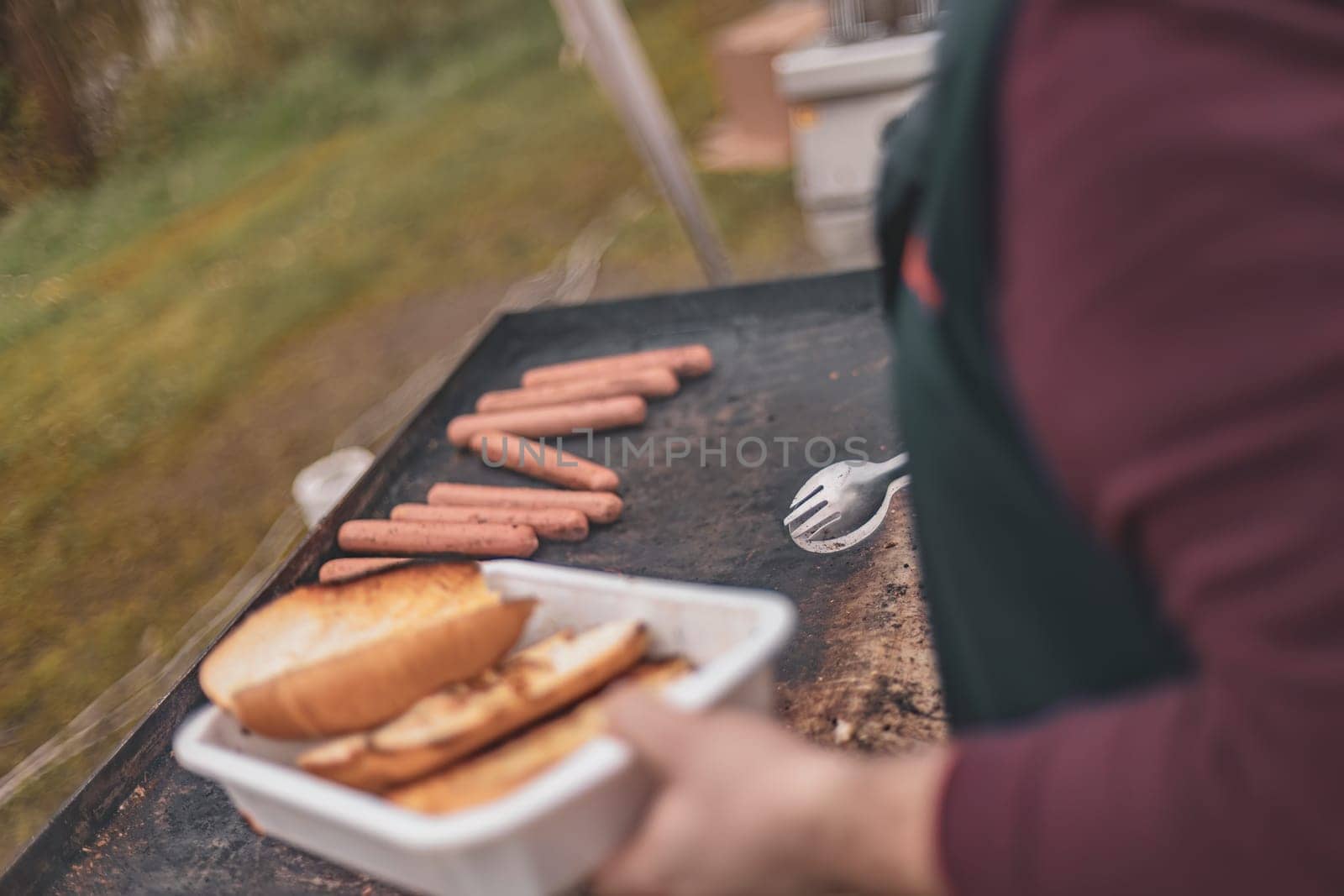Person Holding Tray of Hot Dogs on Grill by pippocarlot