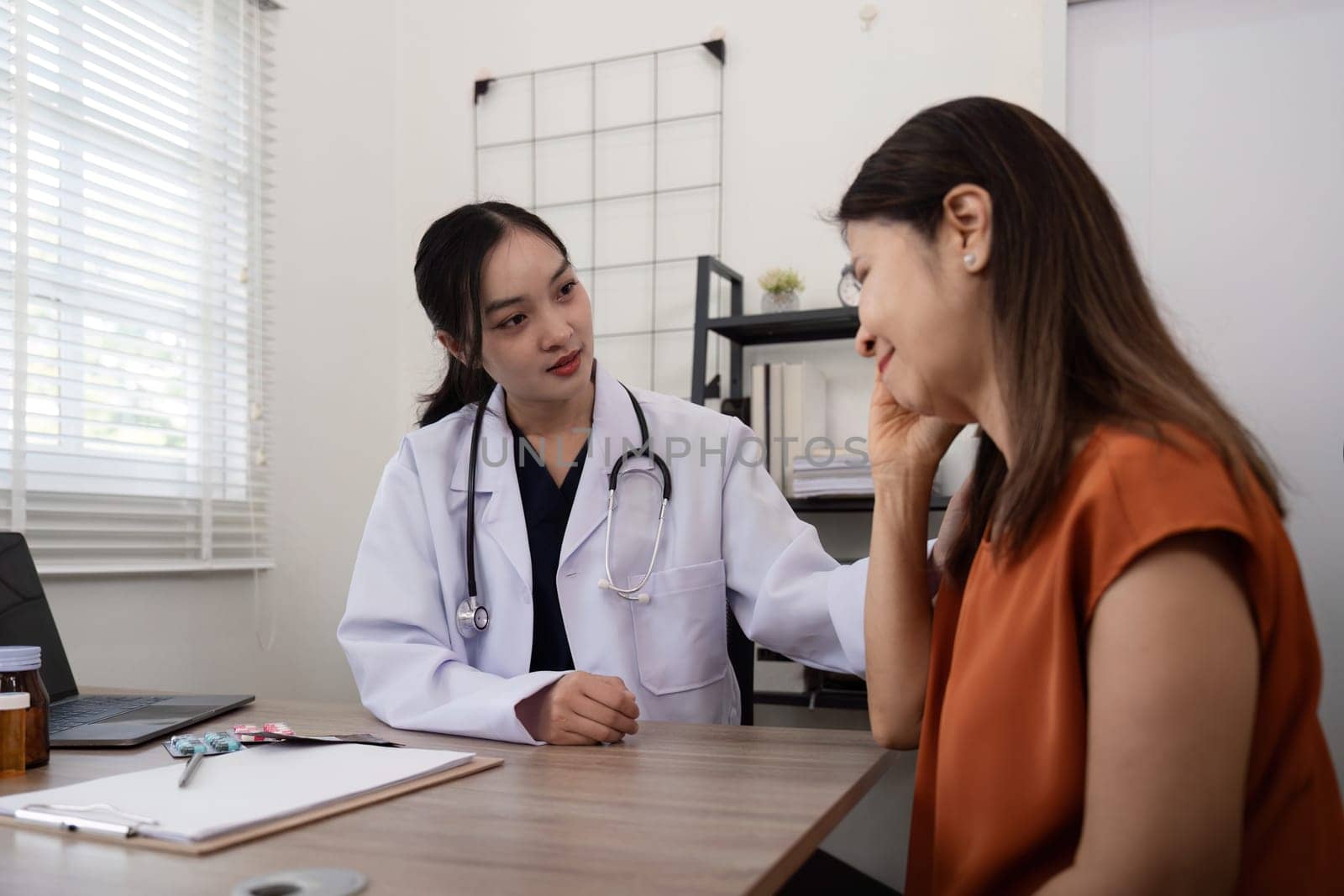 A female doctor asks about the symptom of an elderly female patient who is suffering from stress or headache. and holding the shoulder to encourage the patient.