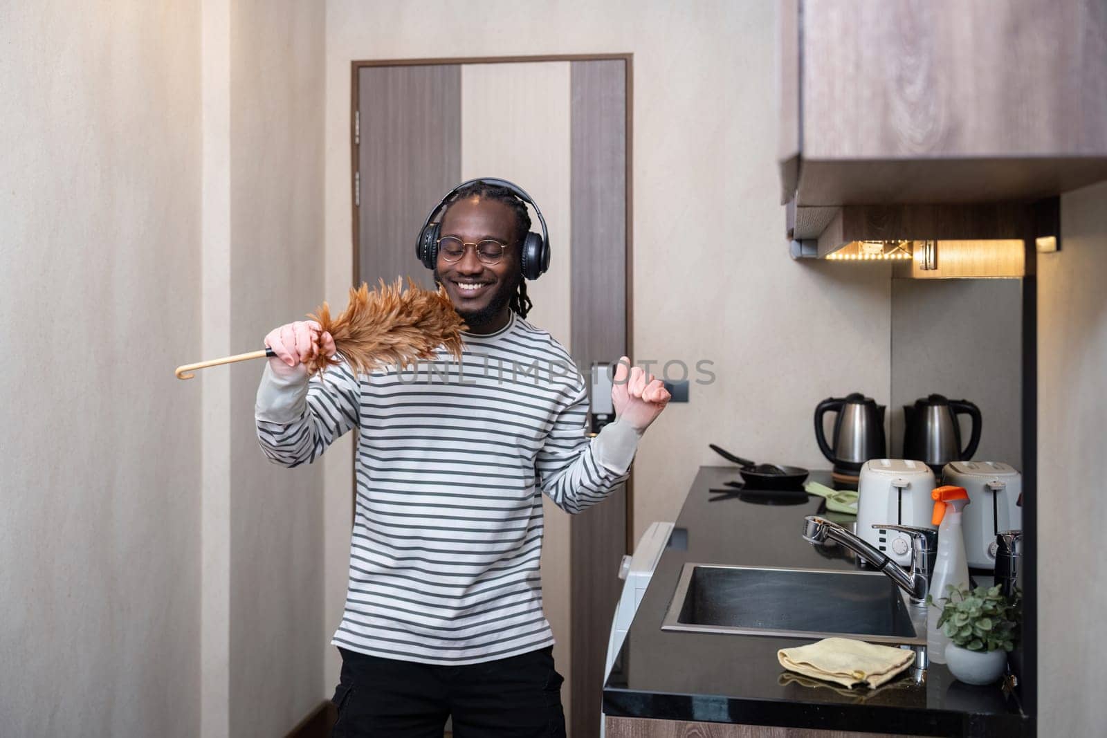 African American man listening to music while cleaning in kitchen by nateemee