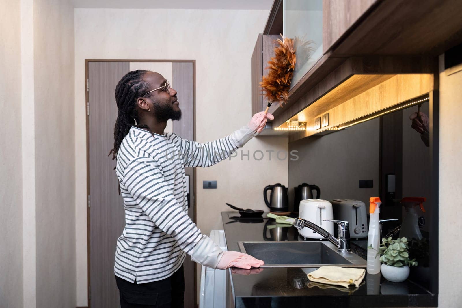 African American man young use duster cleaning in kitchen at home by nateemee