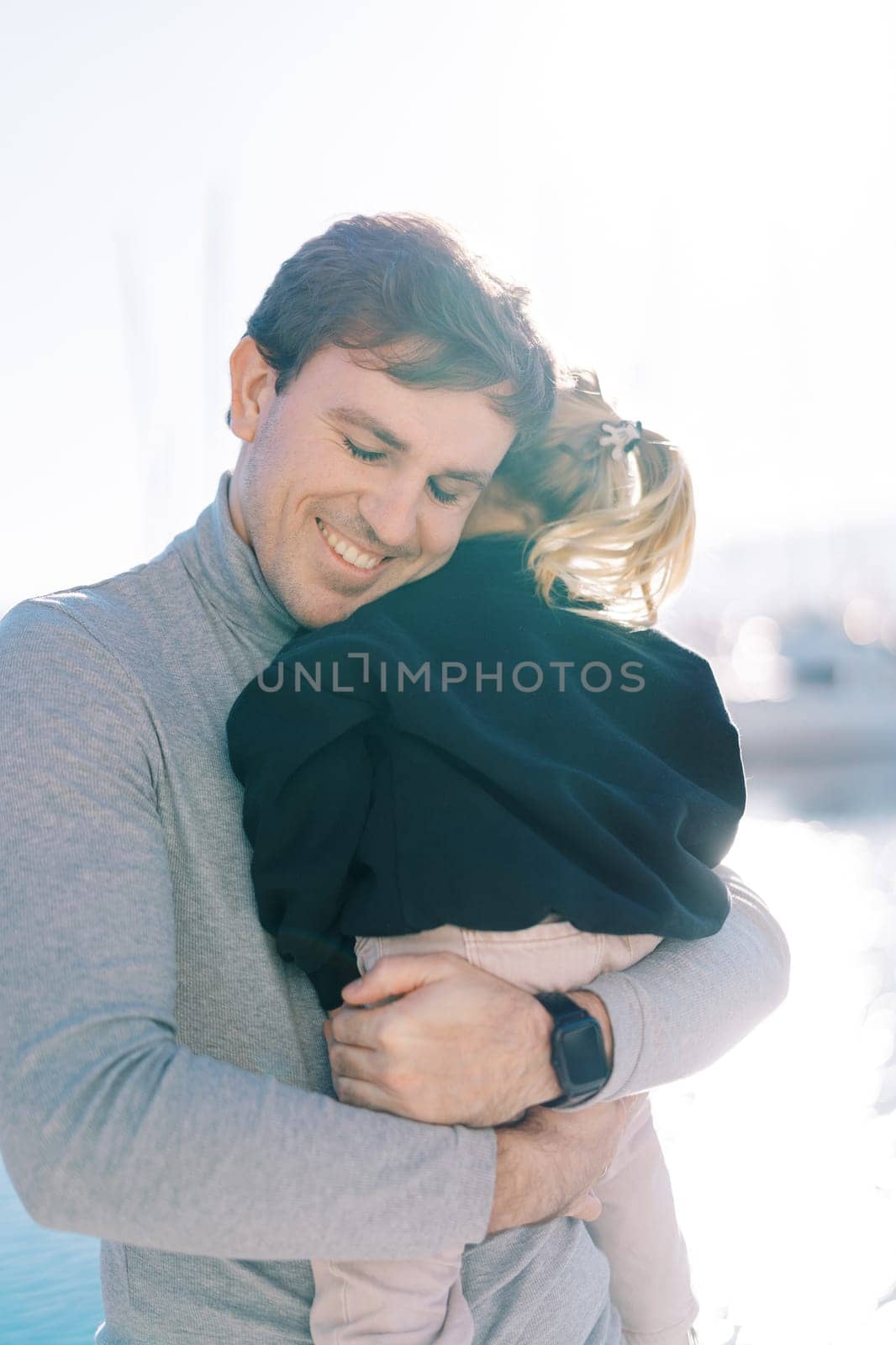 Smiling dad hugs a little girl sitting in his arms on the seashore. High quality photo