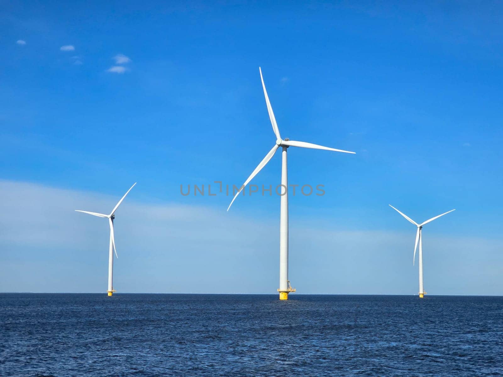 Windmill park in the ocean, view of windmill turbines on a Dutch dike generating green energy electrically, windmills isolated at sea in the Netherlands.