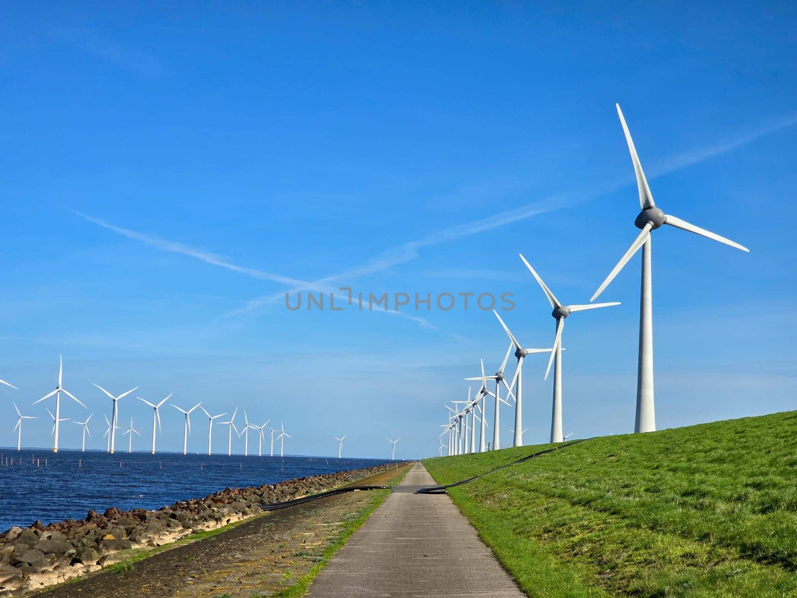 Windmill park in the ocean, view of windmill turbines on a Dutch dike generating green energy electrically, windmills isolated at sea in the Netherlands in Spring