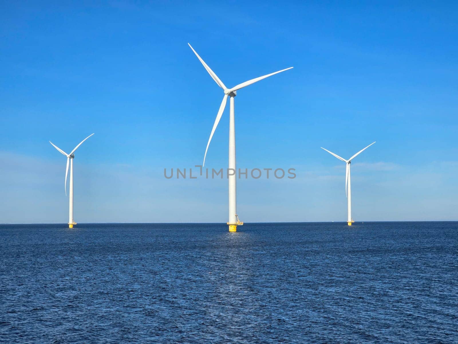Windmill park in the ocean, view of windmill turbines on a Dutch dike generating green energy electrically, windmills isolated at sea in the Netherlands. Energy transition