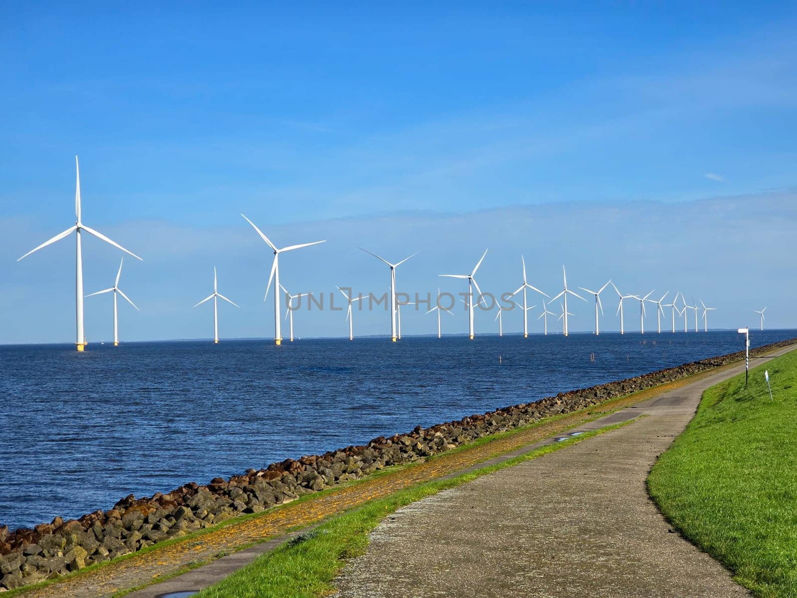 Windmill park in the ocean, view of windmill turbines on a Dutch dike, windmills isolated at sea in the Netherlands. Energy transition, zero emissions, carbon neutral, Earth day concept