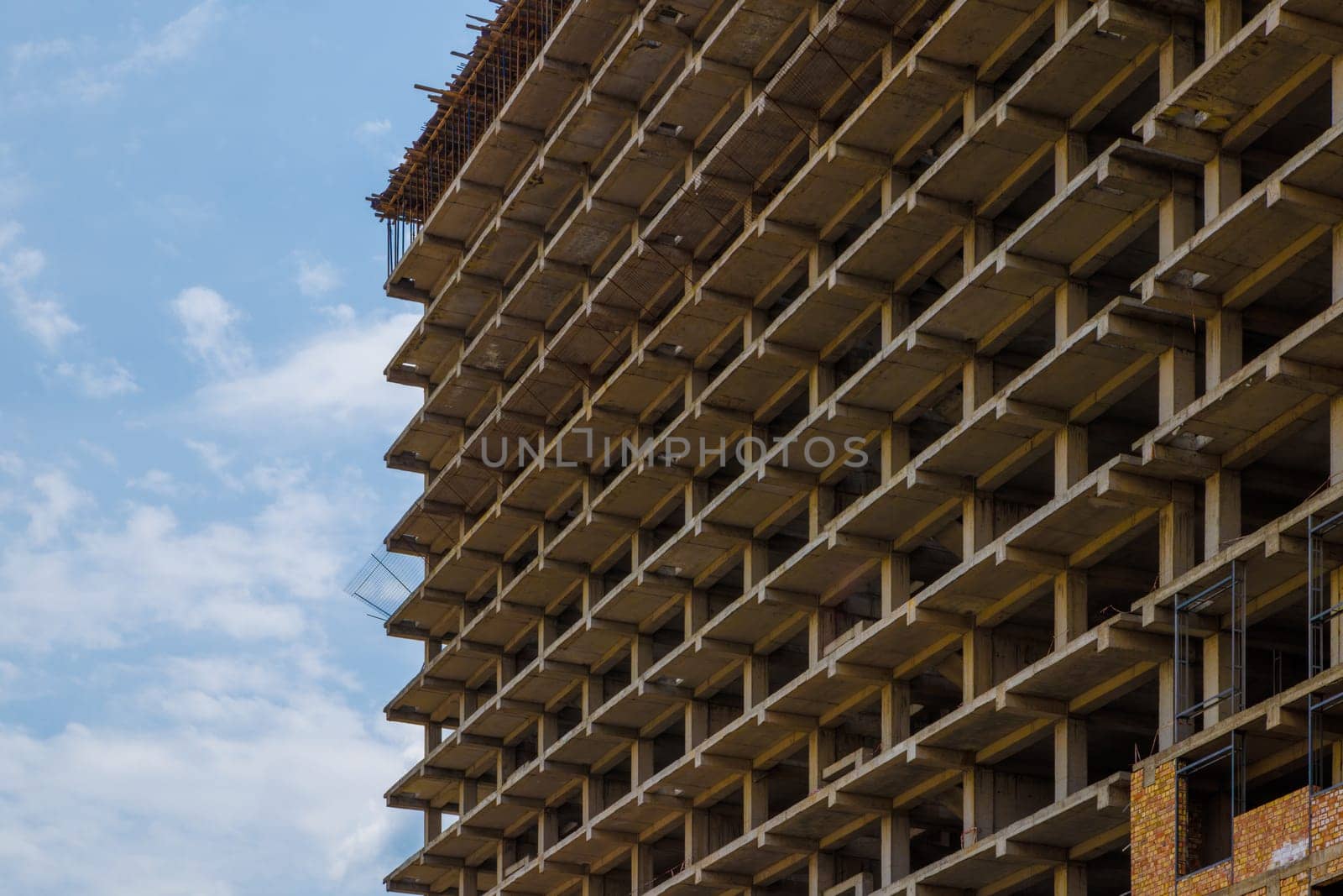 High-rise apartment building under construction against a blue sky with simple square reinforced concrete urban design.