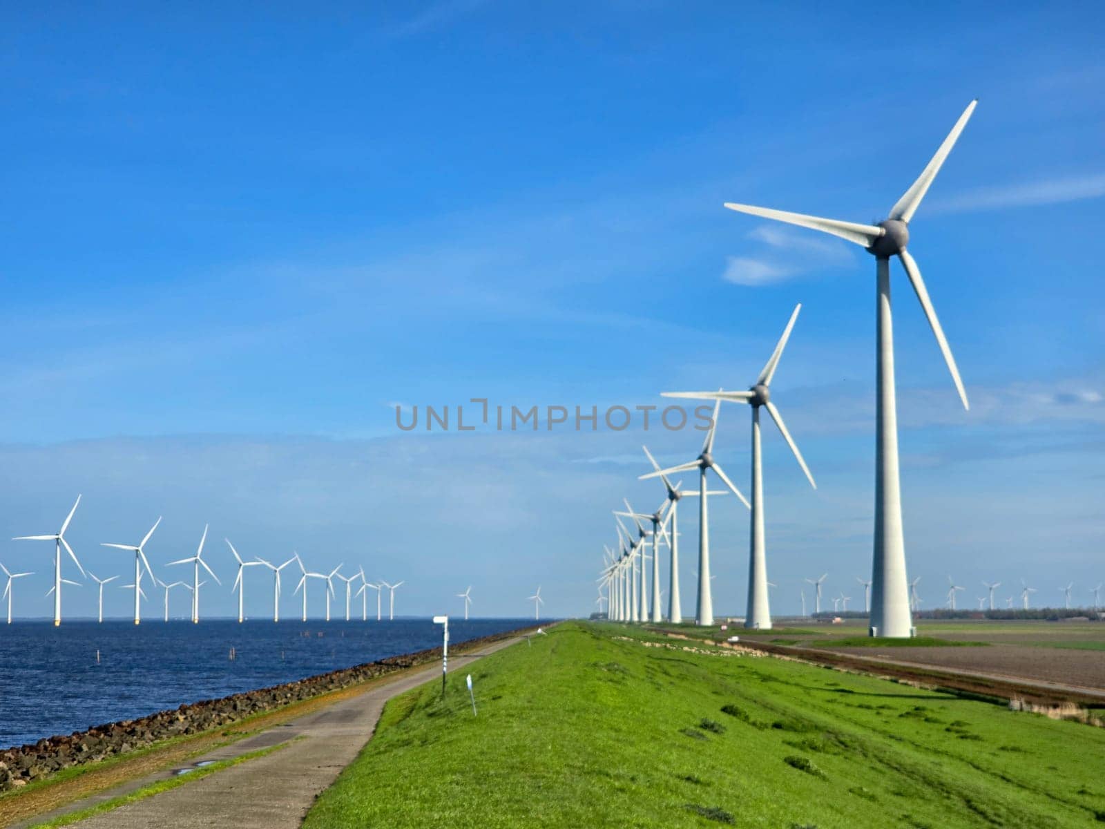 windmill turbines on a Dutch dike generating green energy electrically, windmills isolated at sea in the Netherlands. Energy transition, zero emissions, carbon neutral, Earth day concept