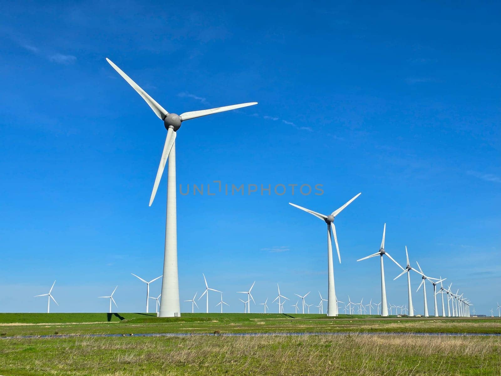 Windmill park in the meadow with a blue sky, view of windmill turbines on a Dutch dike generating green energy electrically, windmills isolated at sea in the Netherlands.