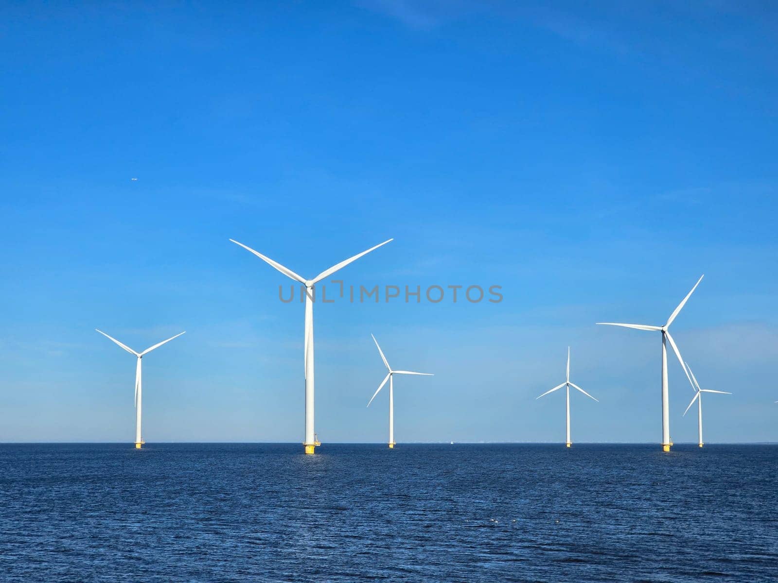 Windmill park in the ocean, view of windmill turbines on a Dutch dike generating green energy electrically, windmills isolated at sea in the Netherlands with a blue sky on a sunny day