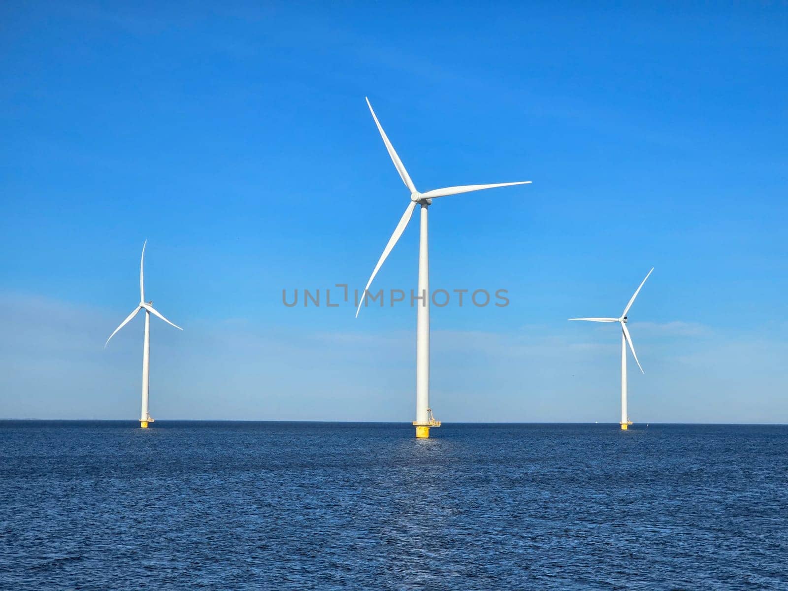 Windmill park in the ocean, view of windmill turbines on a Dutch dike generating green energy electrically, windmills isolated at sea in the Netherlands. Energy transition, zero emissions