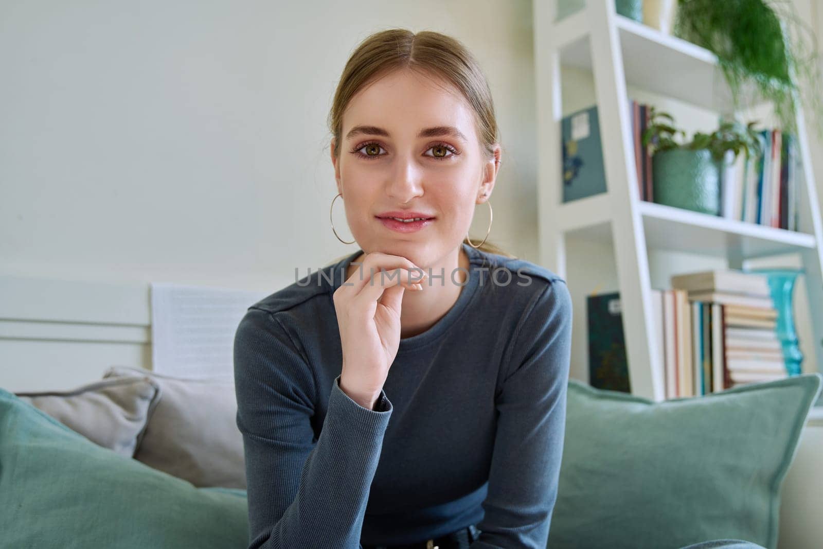 Portrait of beautiful happy smiling teenage girl looking at camera, sitting on couch at home. Age 16,17,18 years, lifestyle, youth concept