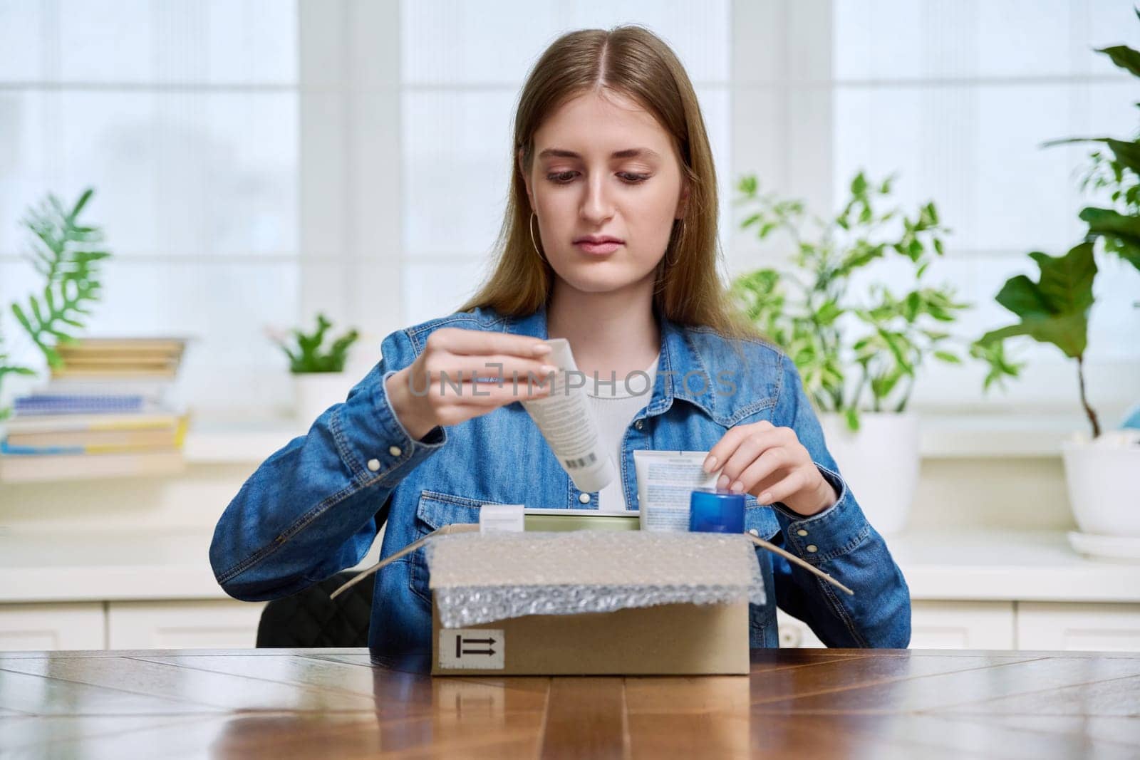 Young female customer sitting at home unpacking cardboard box with online purchases by VH-studio