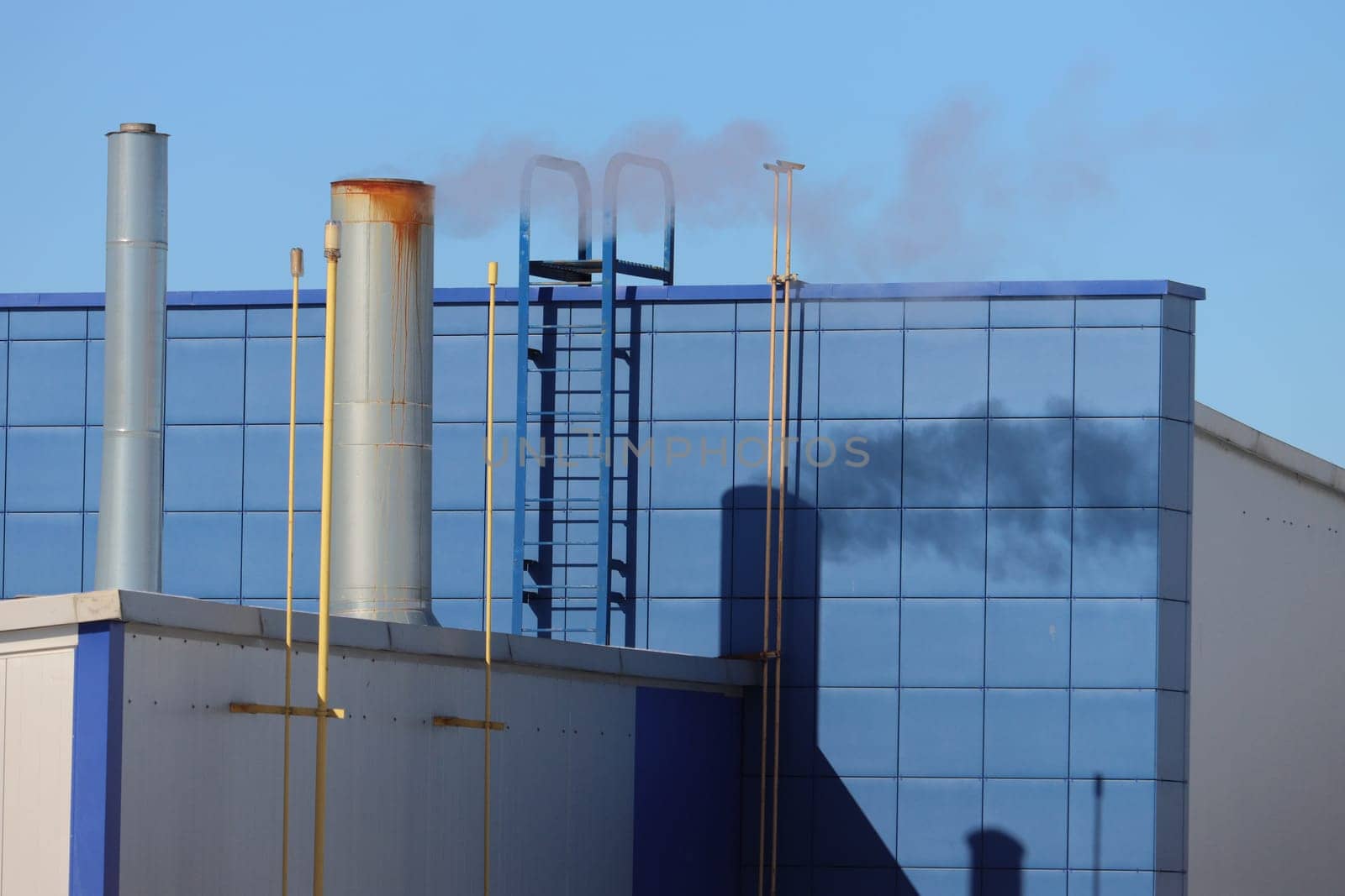 Industrial chimney, low angle view. Chimney with smoke, stairs, wall, building facade in blue.