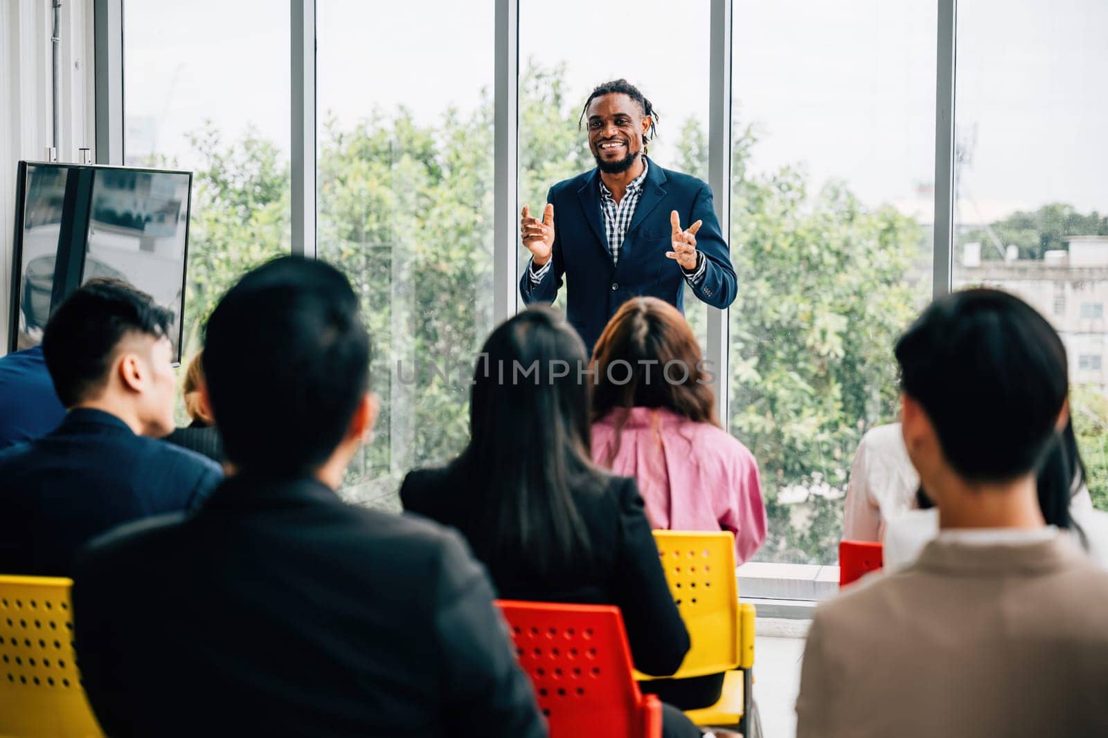 A diverse group of businesspeople convenes in an office meeting. Seated colleagues exchange thoughts, while male and female managers stand, promoting effective teamwork. by Sorapop