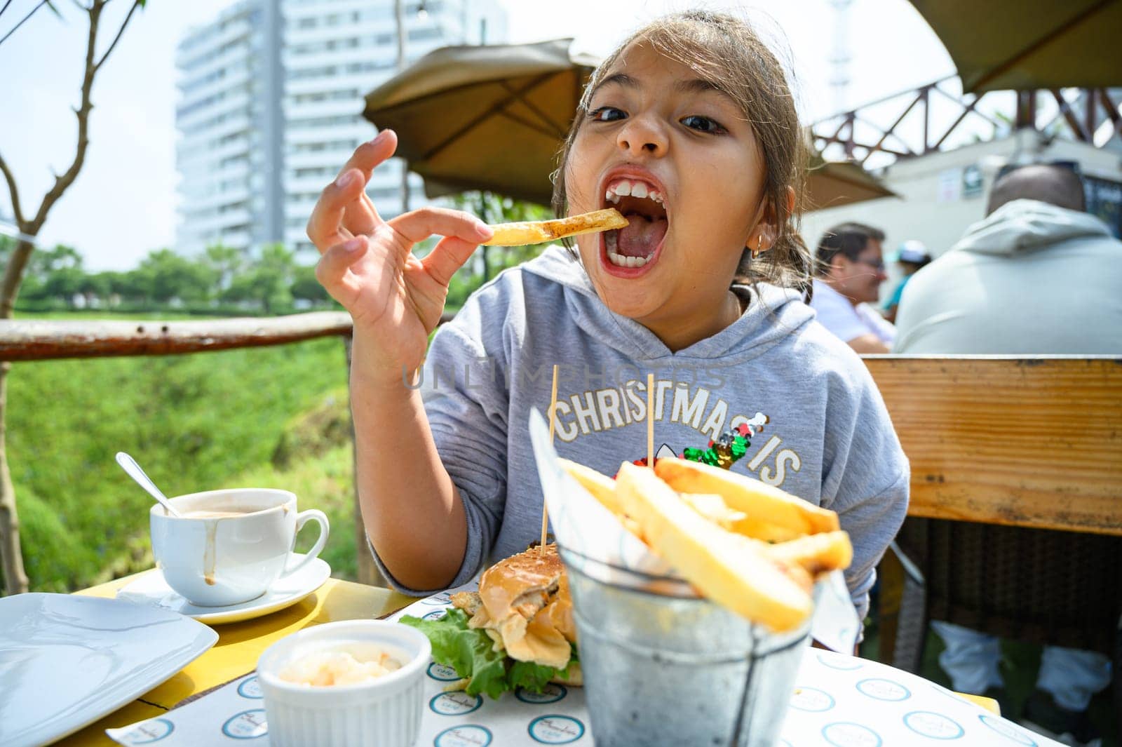 little girl has breakfast in a cafe, eats hamburger and french fries, drinks chocolate